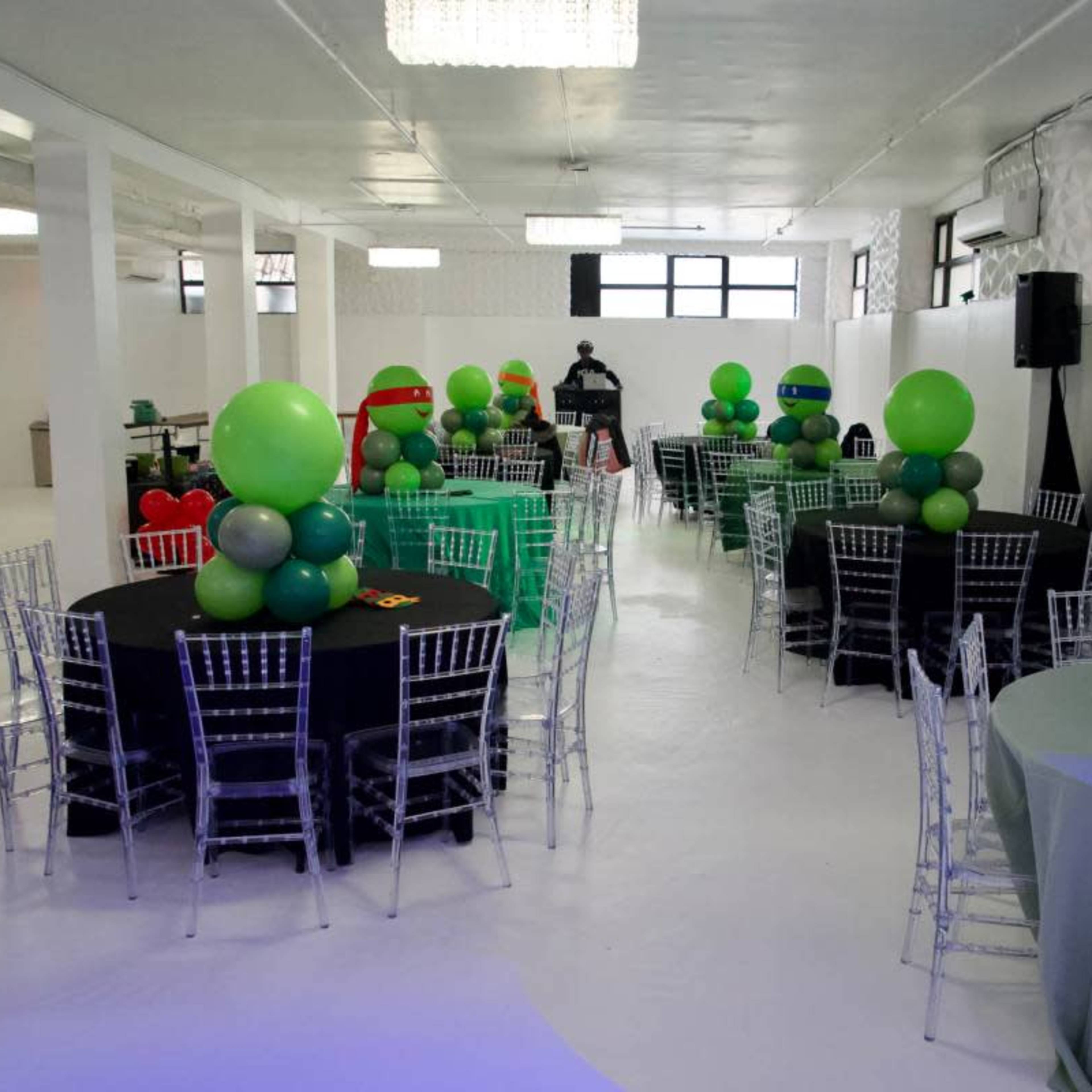 A party venue decorated with colorful balloon arrangements resembling Ninja Turtles, set up with several round tables and chairs.