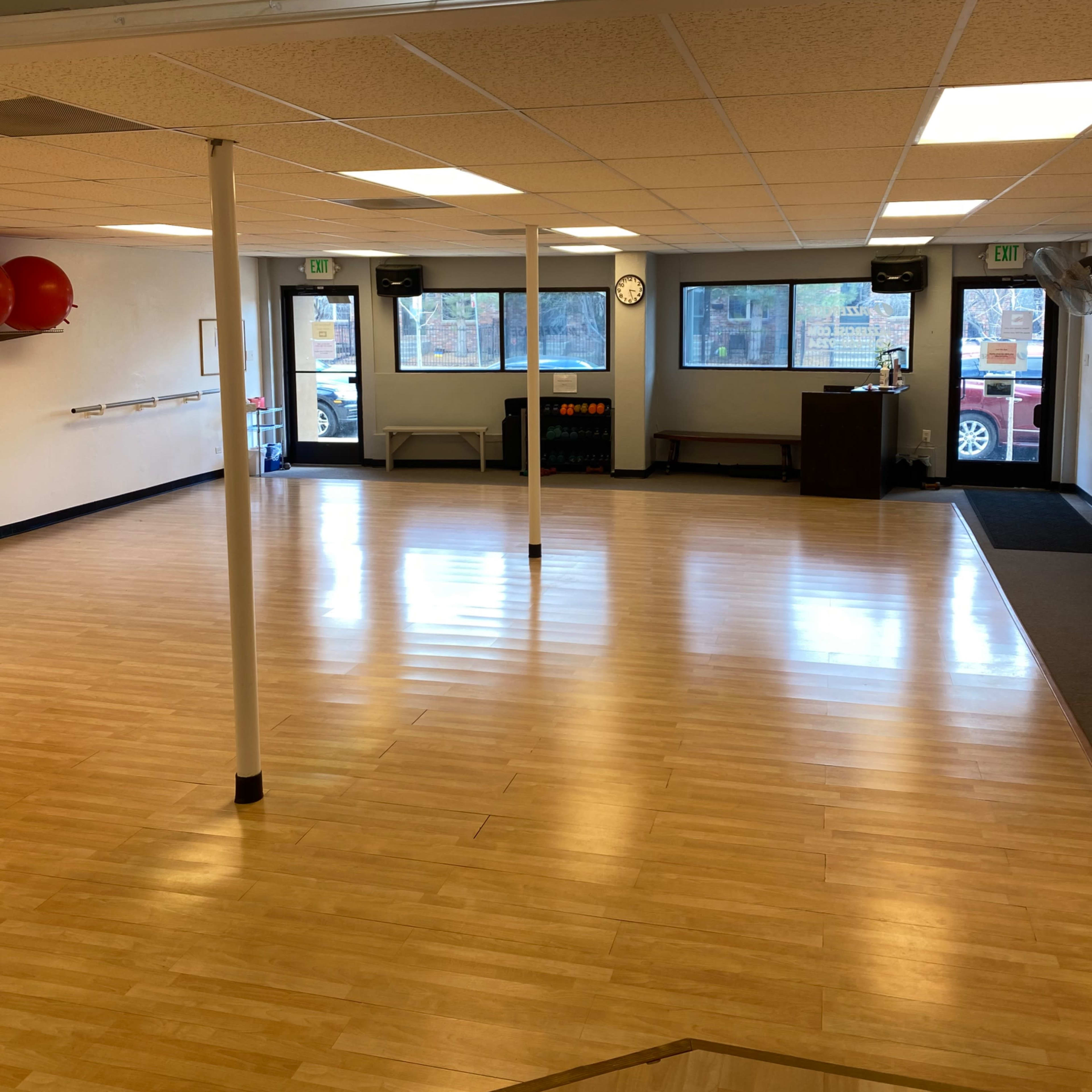 A bright, spacious studio with wooden flooring, large windows, and minimal furnishings.
