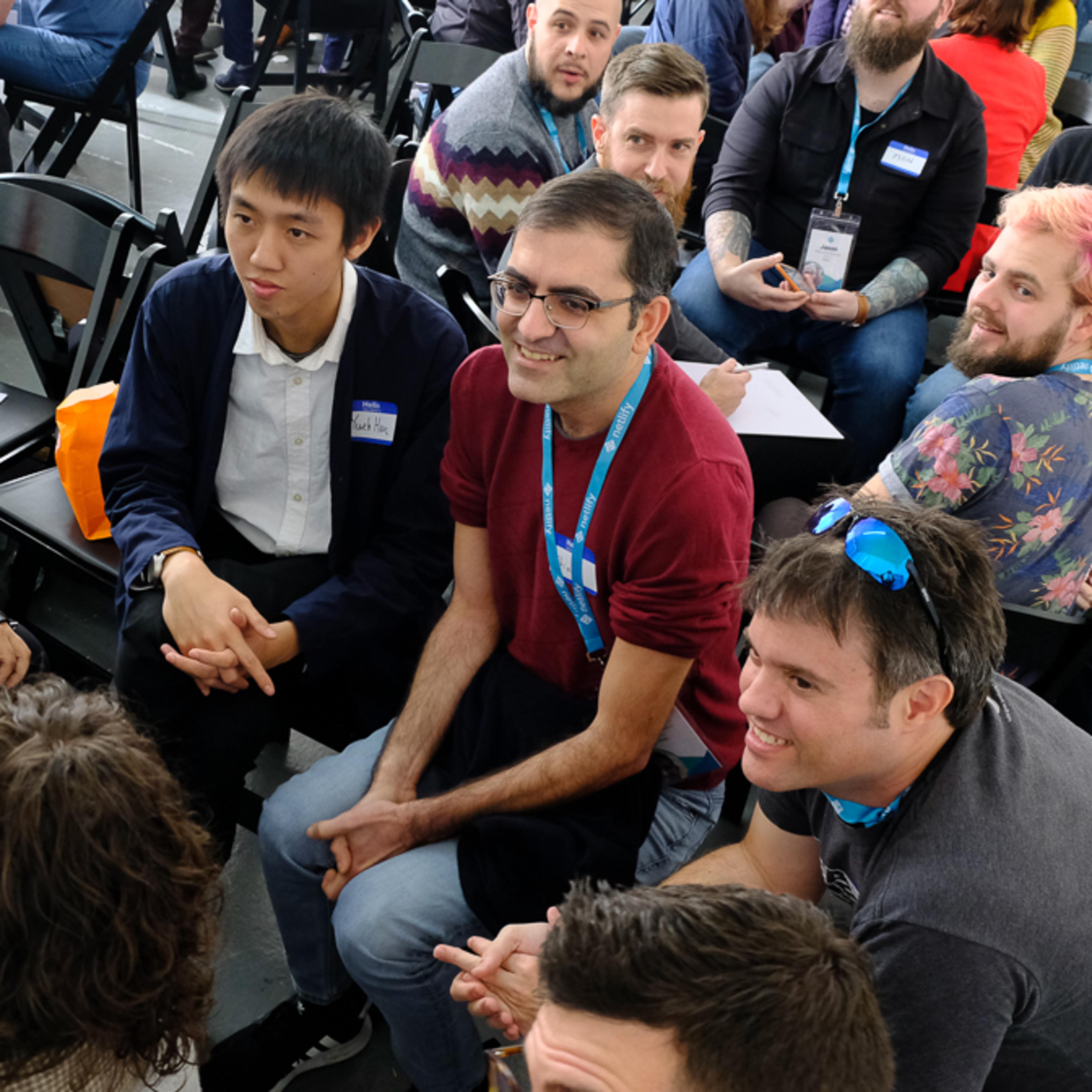 A diverse group of people is seated in a large, open space, engaging in conversation and interaction during a gathering or event.