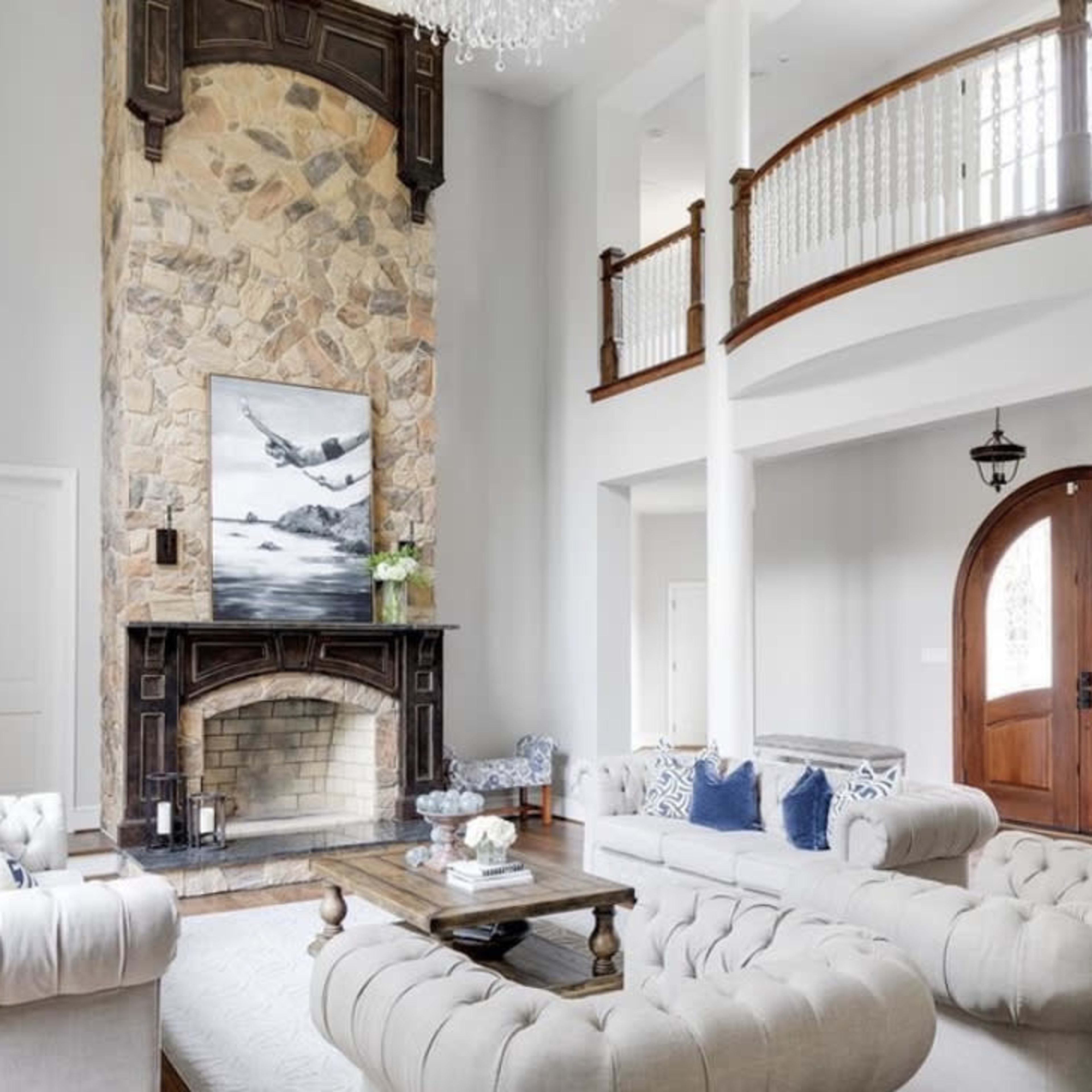 The room features a high ceiling with a stone fireplace at one end, surrounded by large windows and a pair of sofas arranged around a coffee table.