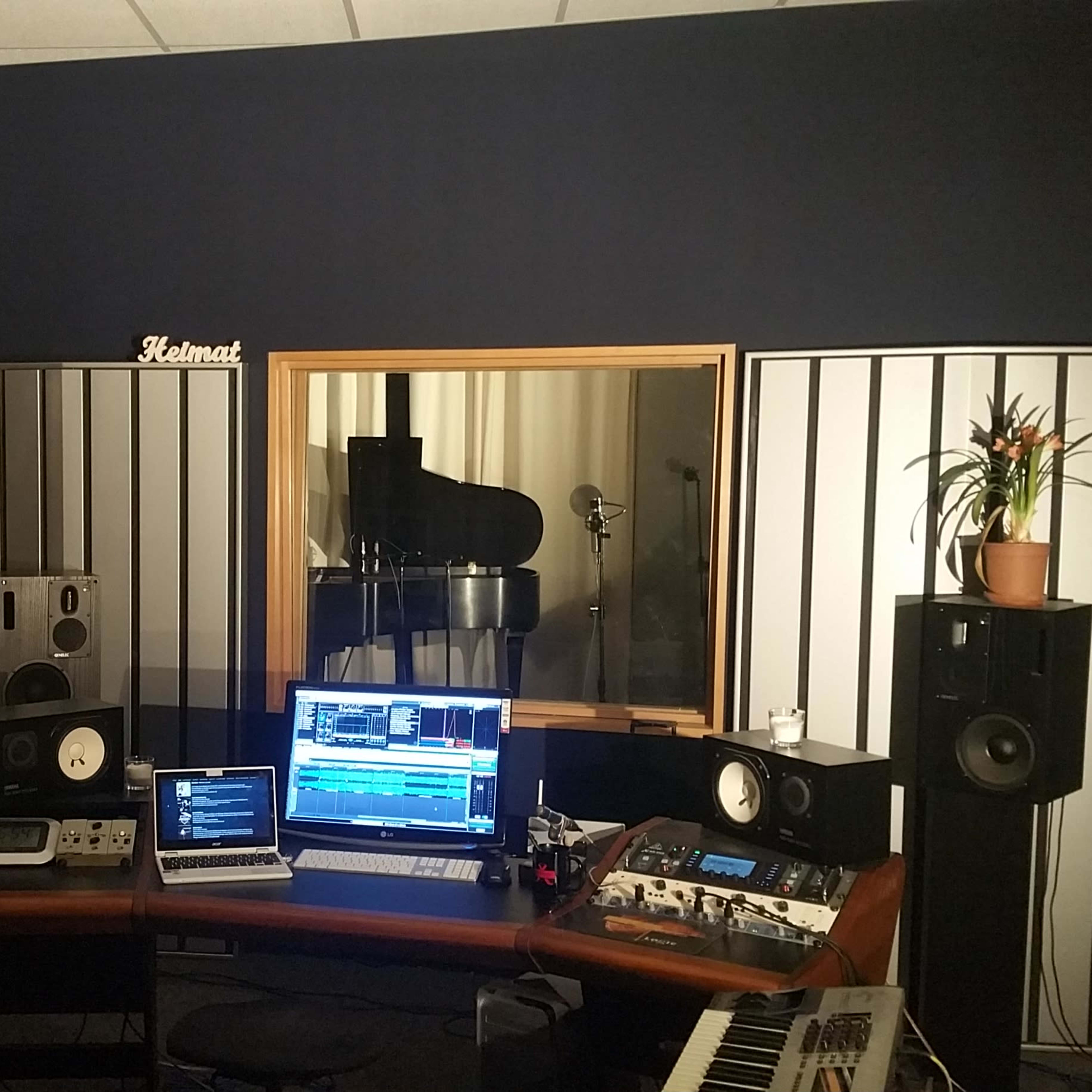 A music studio with a piano, mixing equipment, monitors, and a computer setup on a desk.