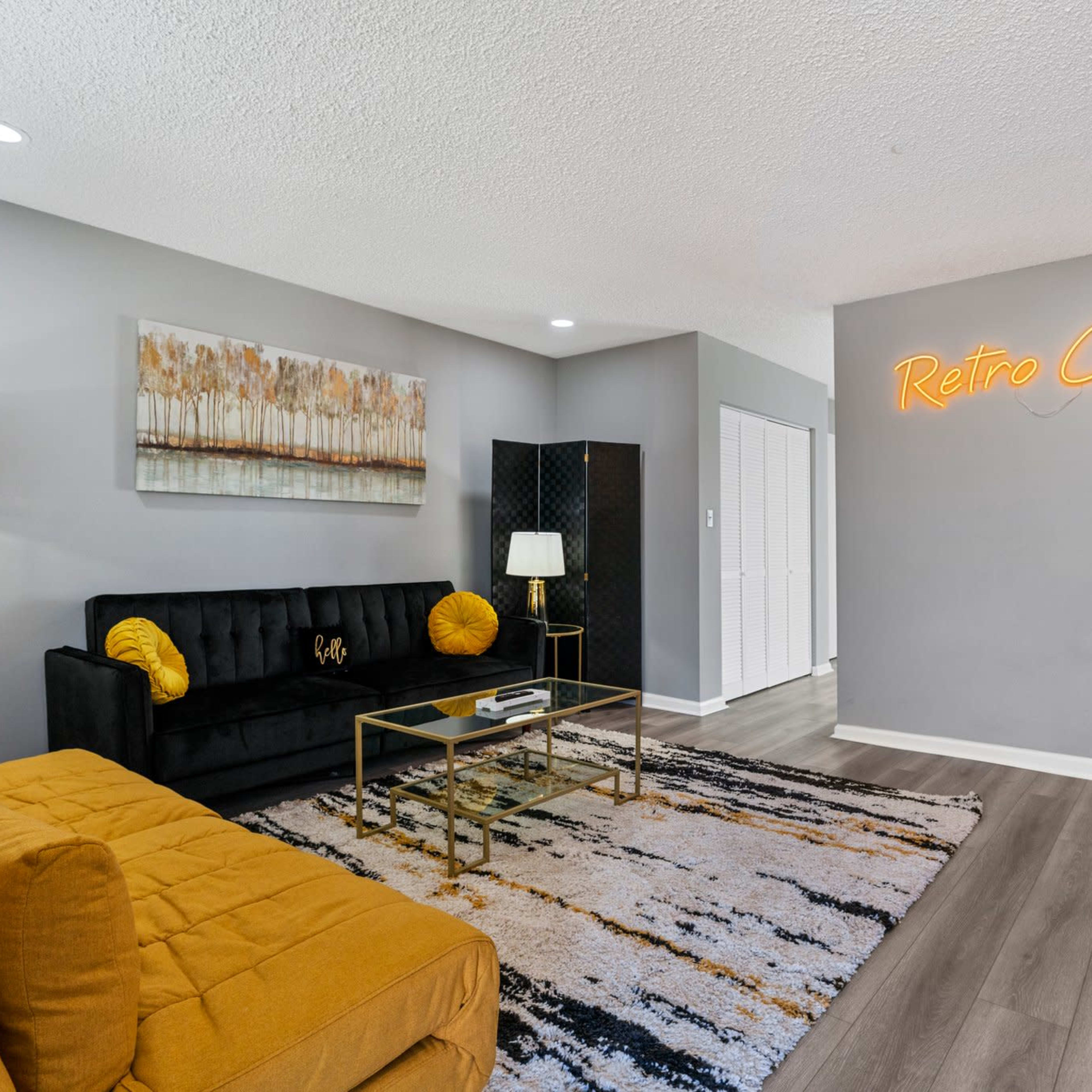 A modern living room with a black sofa, a yellow accent chaise, a gold coffee table, and a neon sign that reads "Retro City" on the wall.
