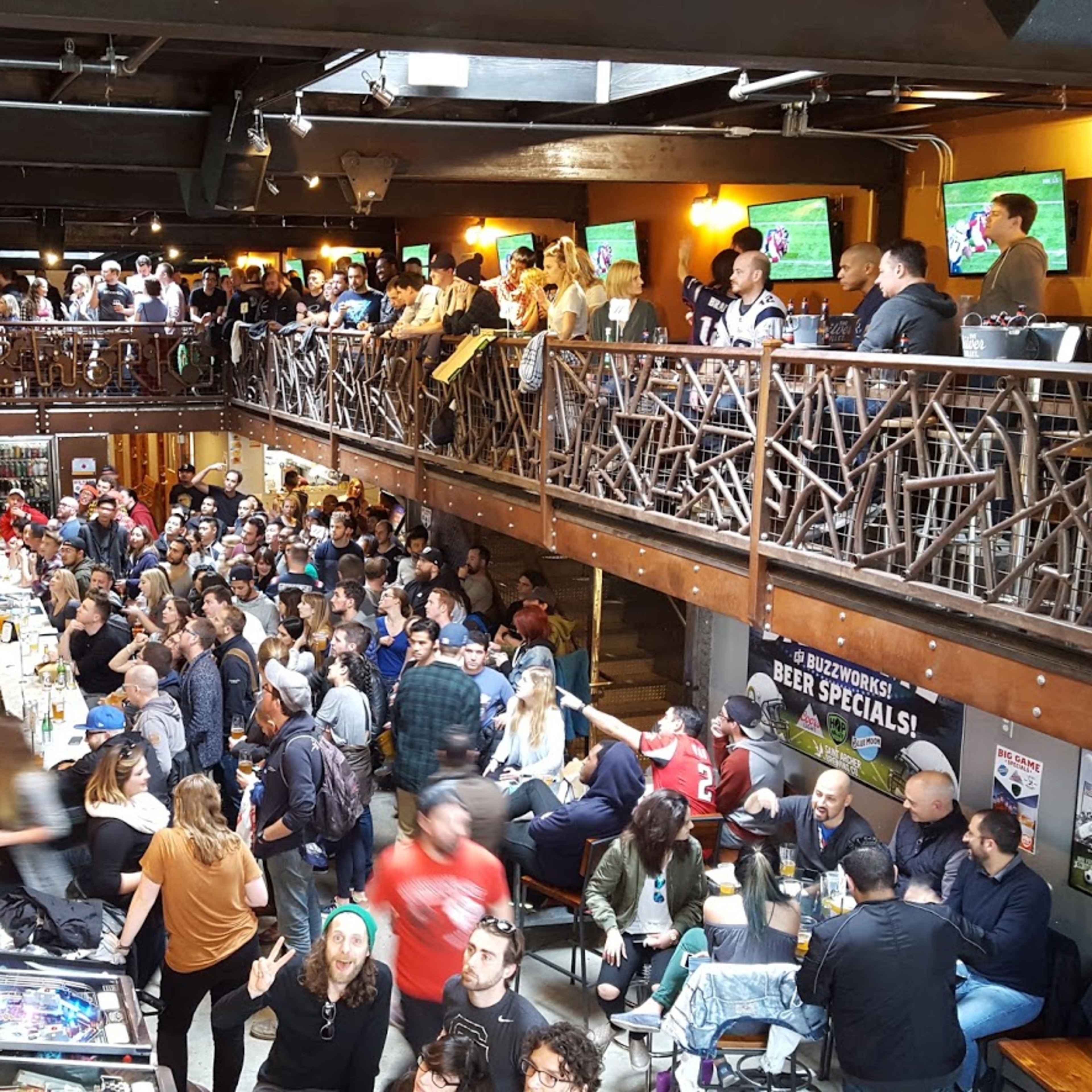 A crowded bar with multiple levels is filled with patrons watching sports on large screens and socializing.