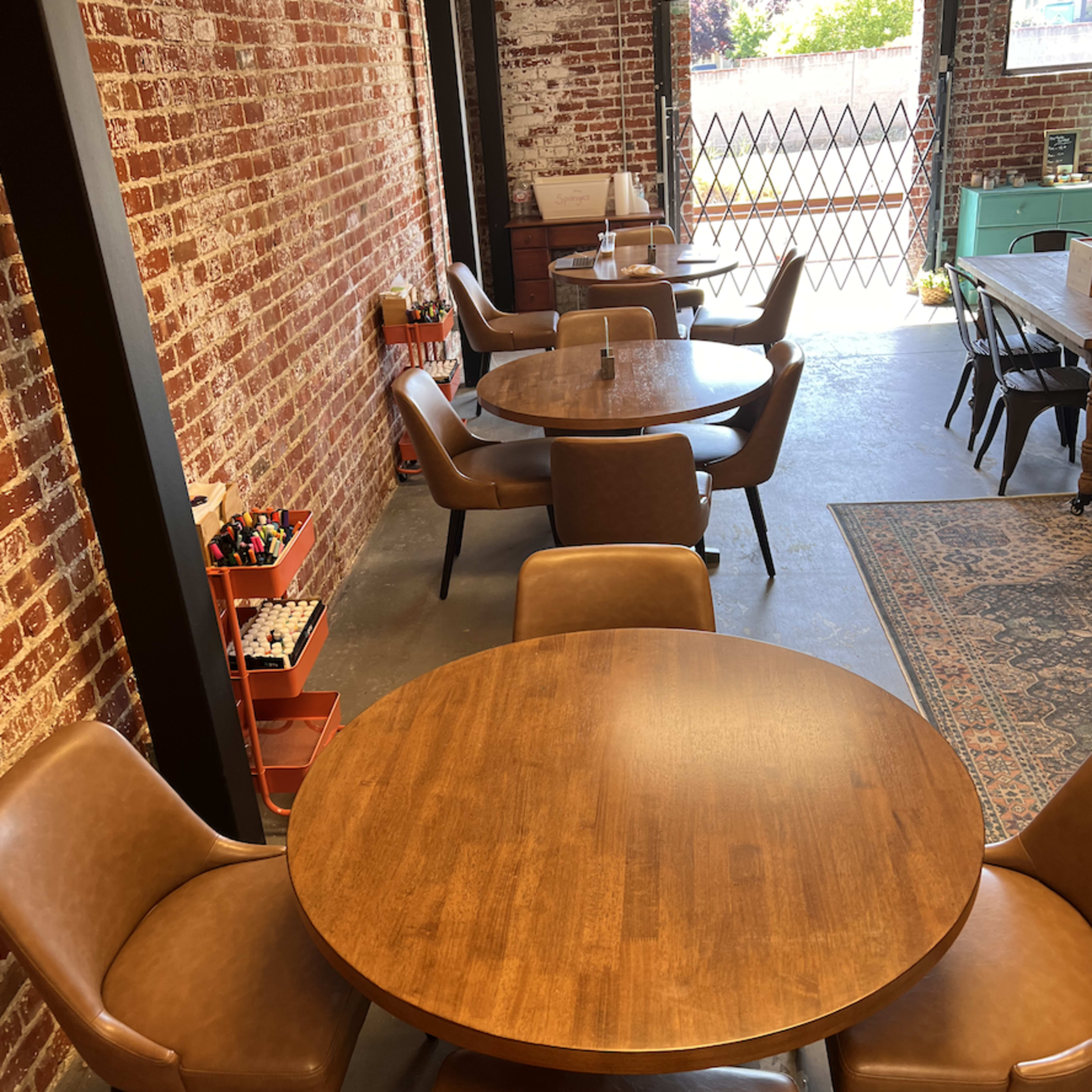 A spacious dining area with wooden tables and brown leather chairs arranged under exposed brick walls.