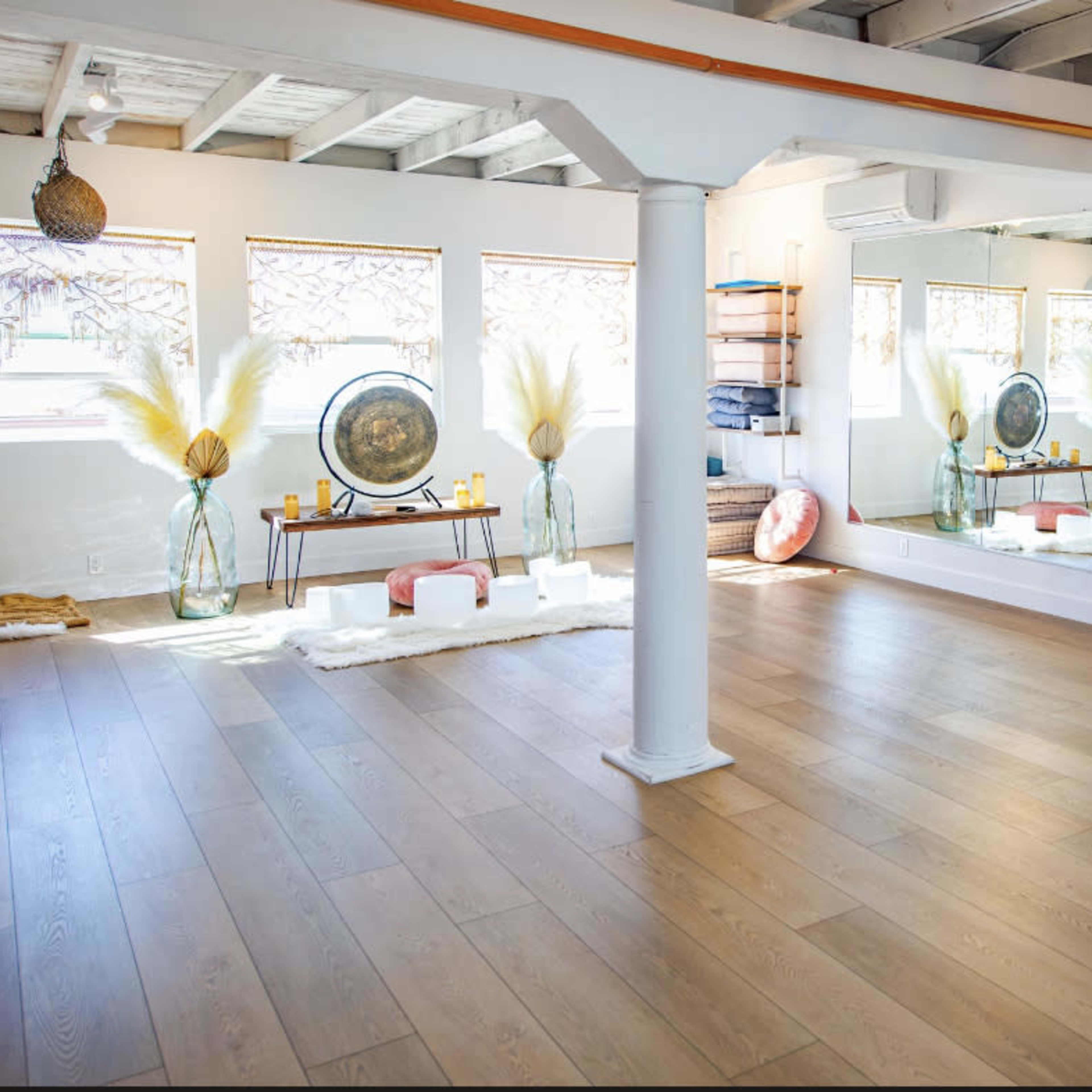 A spacious, well-lit room featuring wooden floors, large mirrors, and decorative items like vases and cushions.