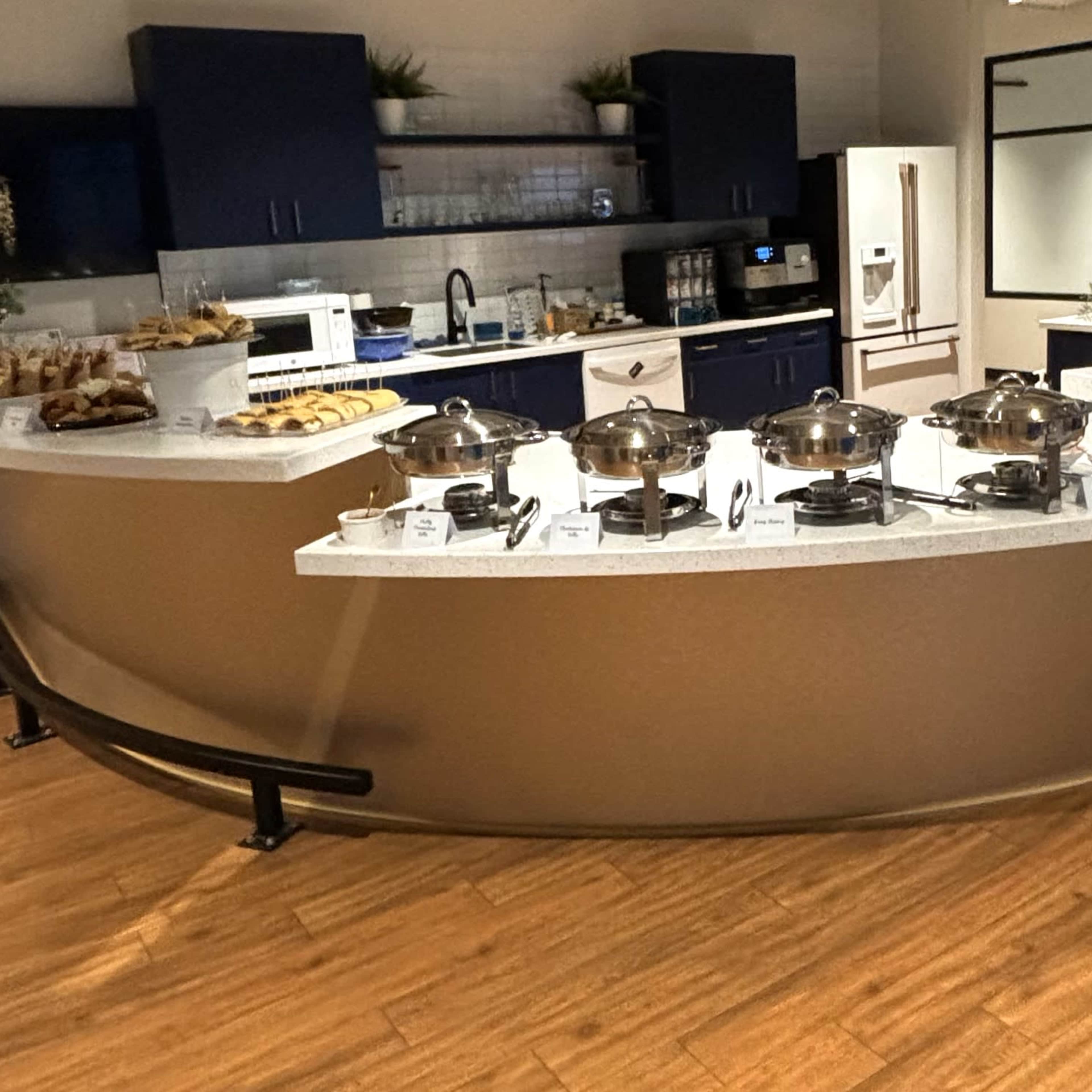 A buffet station filled with various food items and serving dishes arranged on a curved counter in a modern kitchen setting.