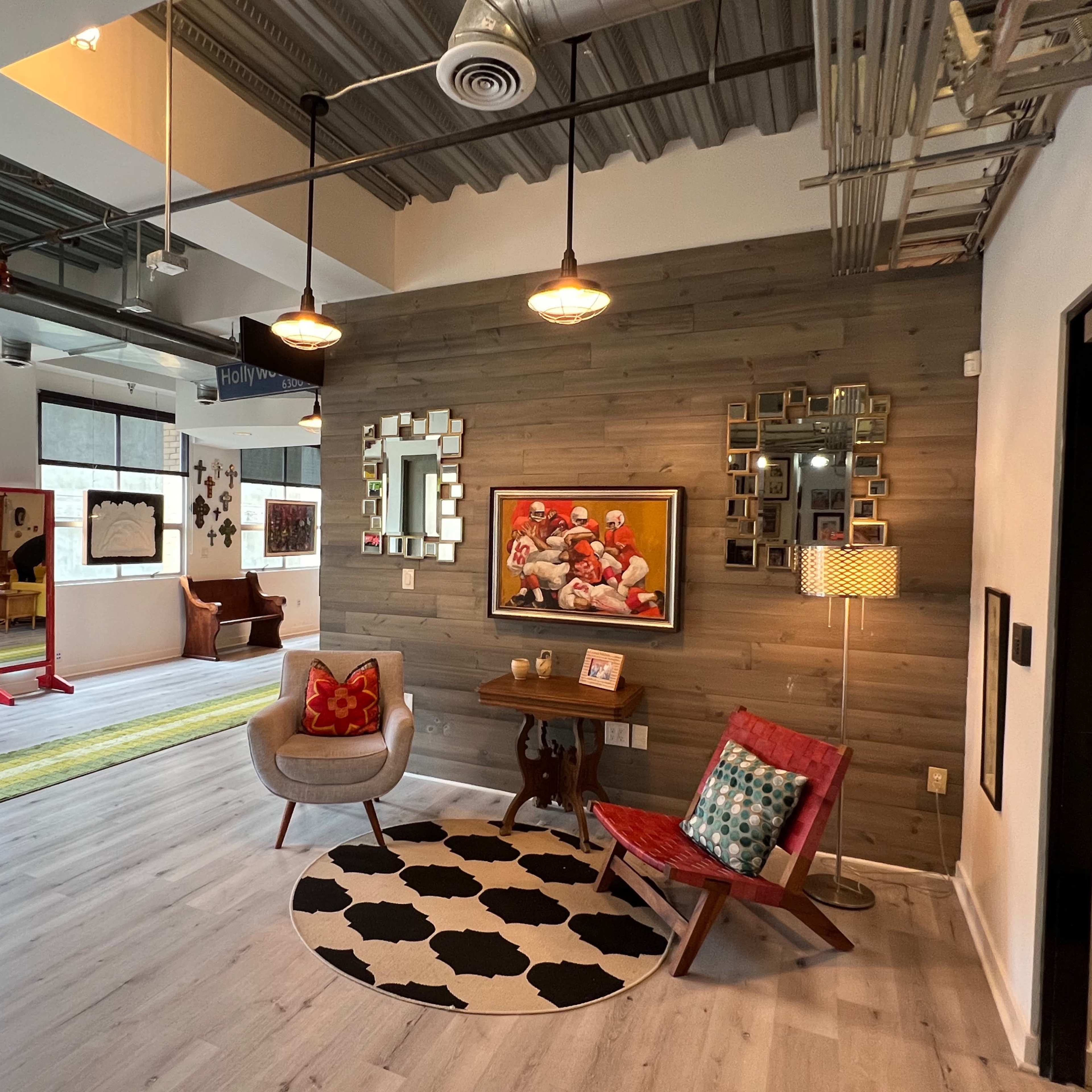 The scene shows a modern interior space with wooden accents, several decorative wall frames, colorful furniture, and patterned rugs.