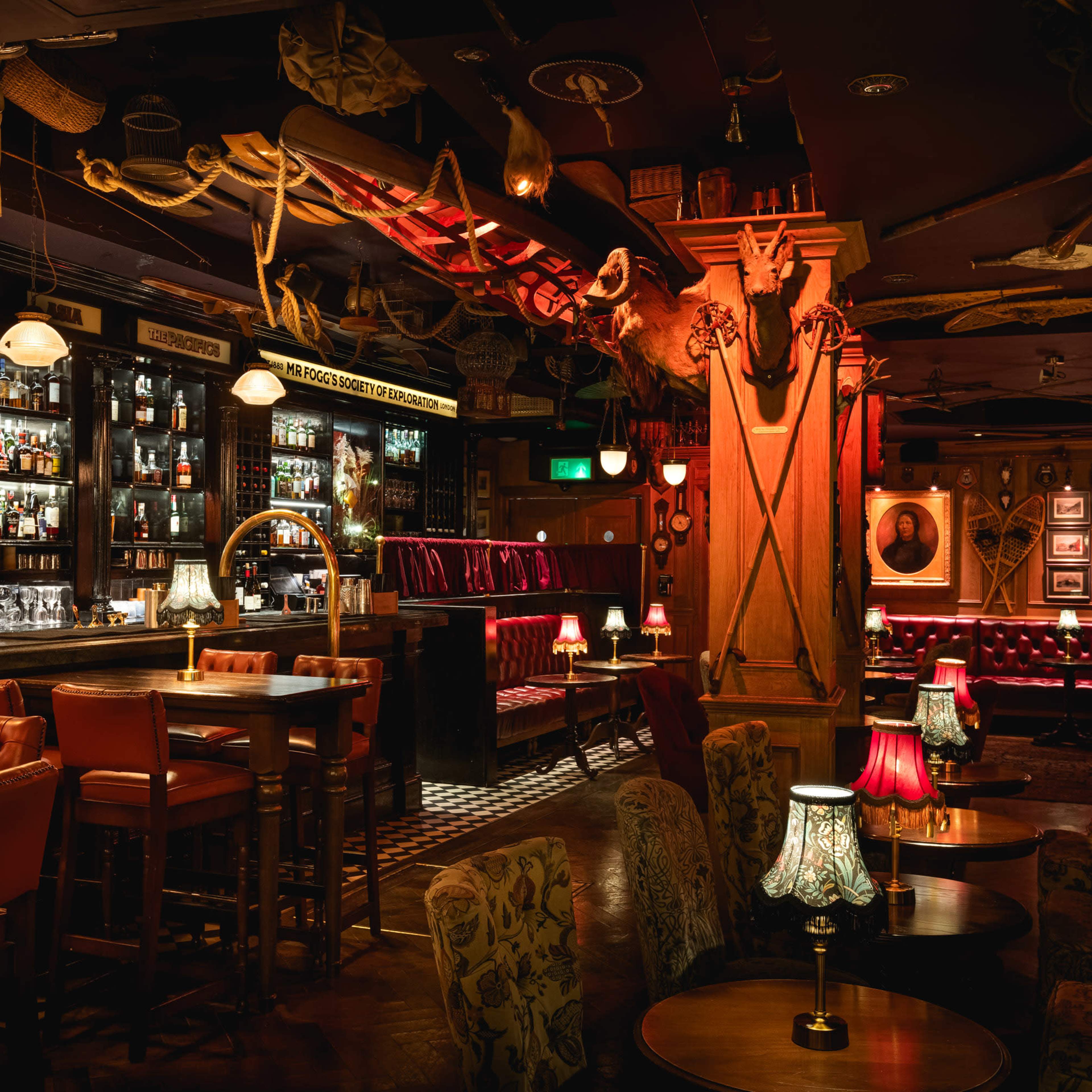 A dimly lit bar with wooden furniture, shelves lined with liquor bottles, and decorative taxidermy on the walls.