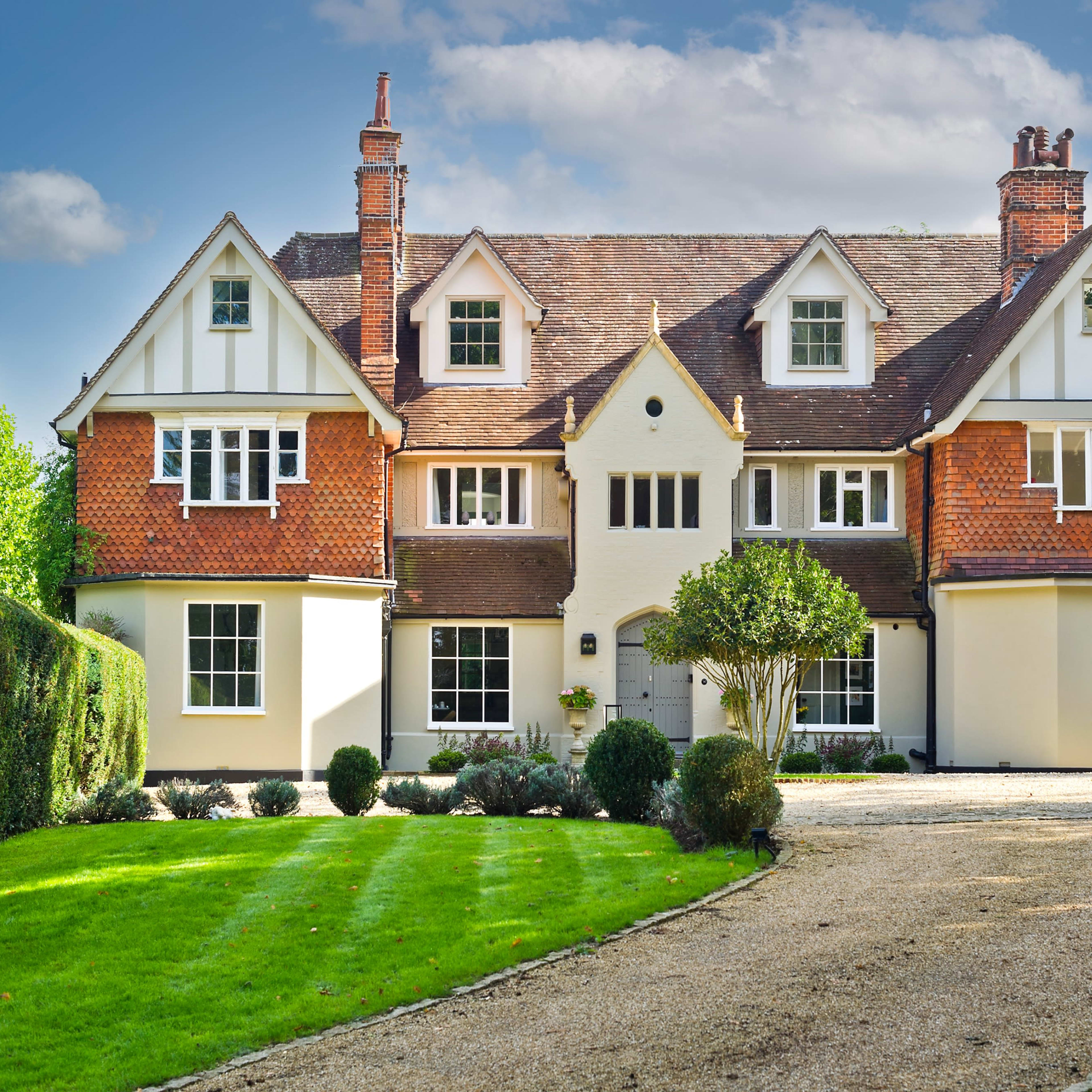 A large, two-story house with a symmetrical facade, characterized by a mix of red brick and white clapboard, set in a landscaped yard with neatly trimmed hedges and a gravel driveway.