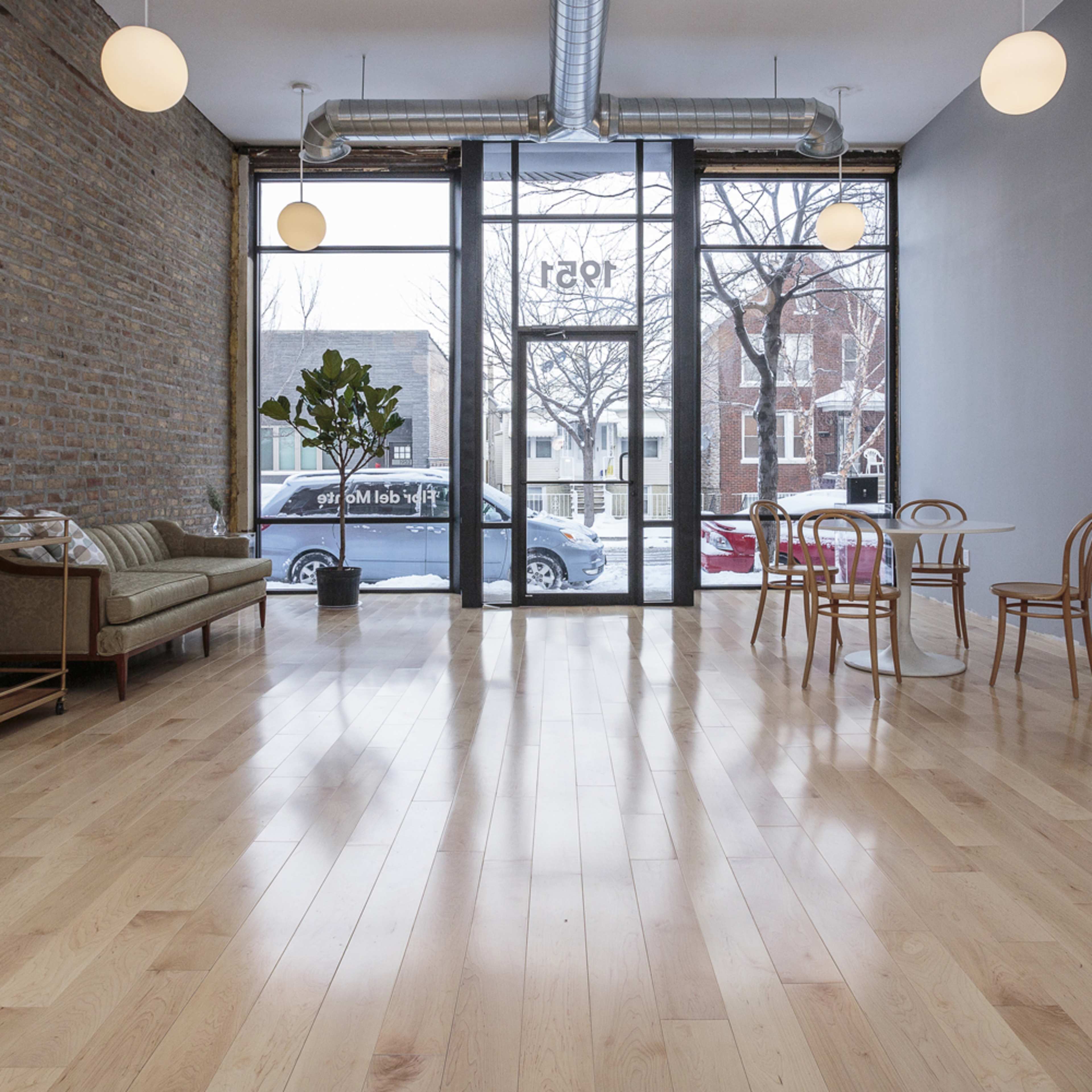 A spacious, empty room with hardwood floors, large windows, and a mix of modern furniture including a sofa, dining table, and chairs.
