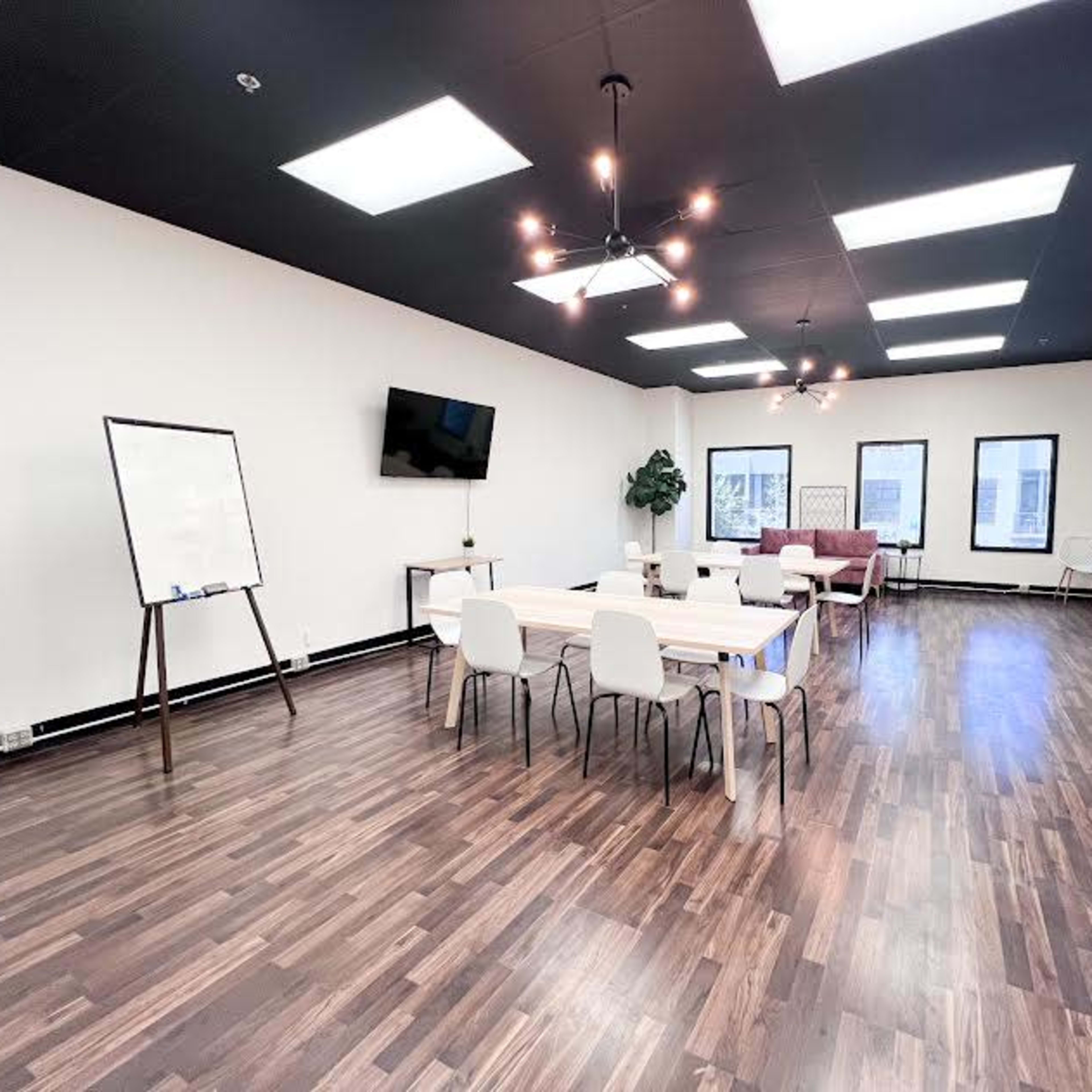 A modern, well-lit meeting room with a large table, several chairs, a whiteboard, a television mounted on the wall, and a couch.