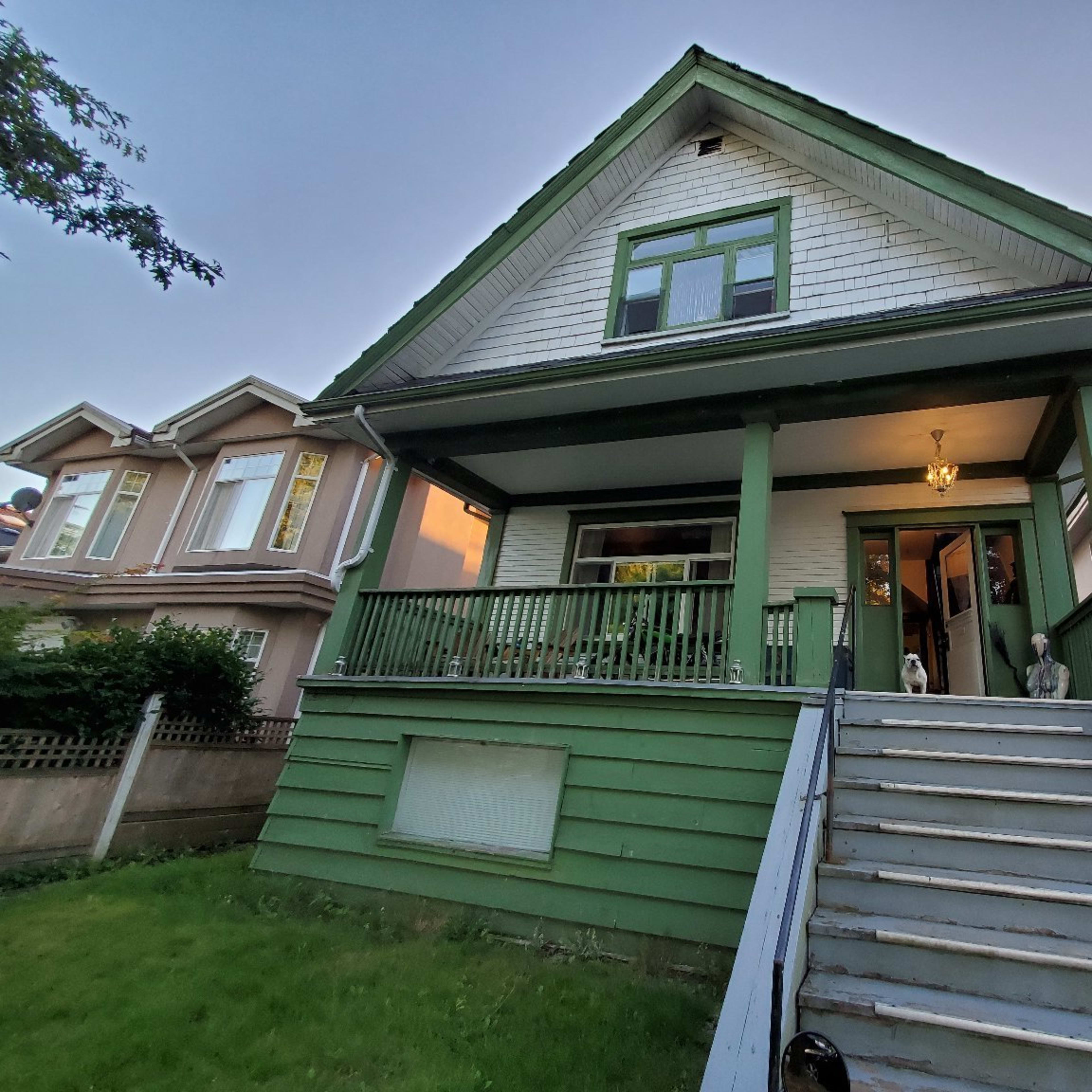 A green, two-story house with a front porch and white shingle accents is visible, surrounded by well-maintained lawns and neighboring homes.