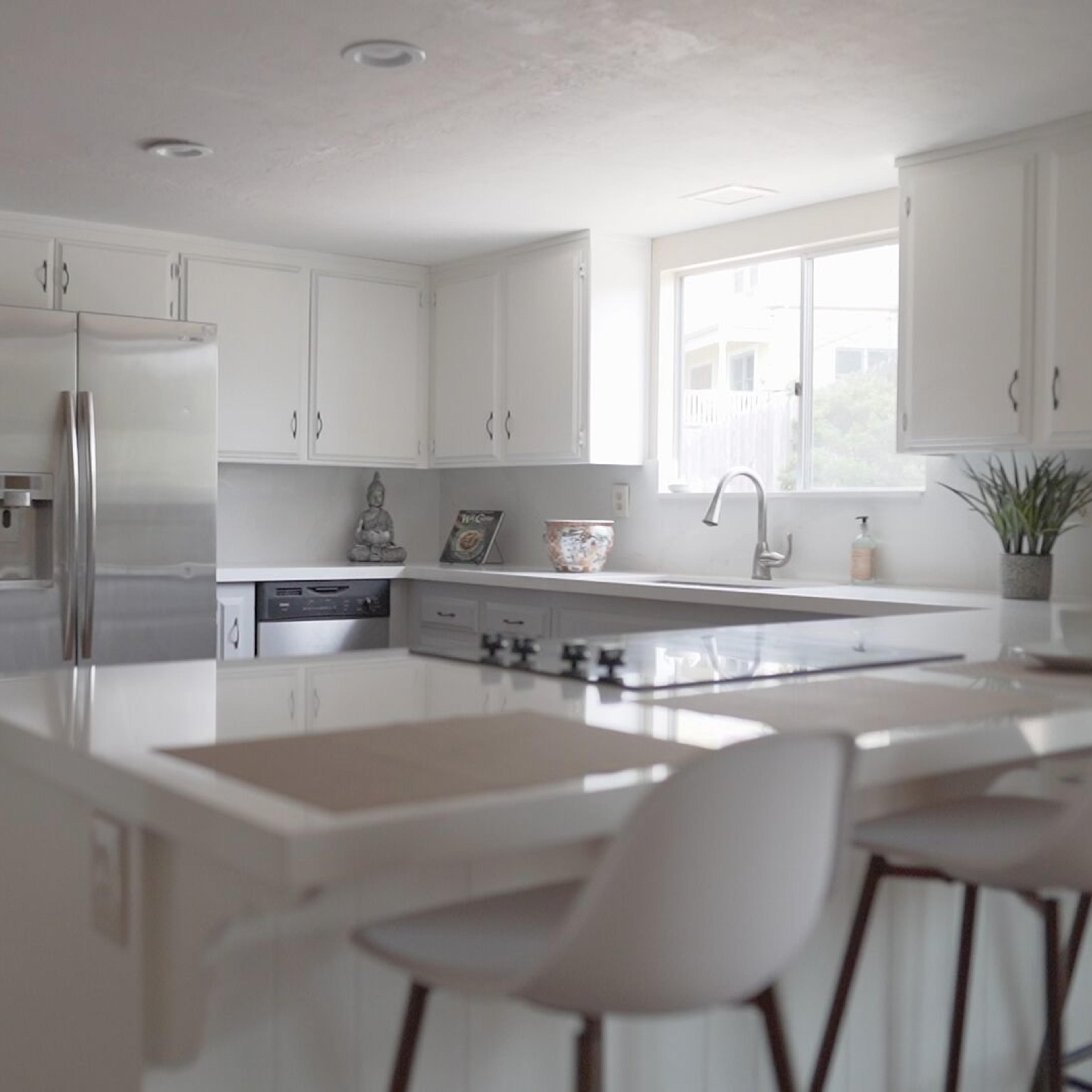 A modern kitchen features white cabinetry, stainless steel appliances, and a large island with seating.