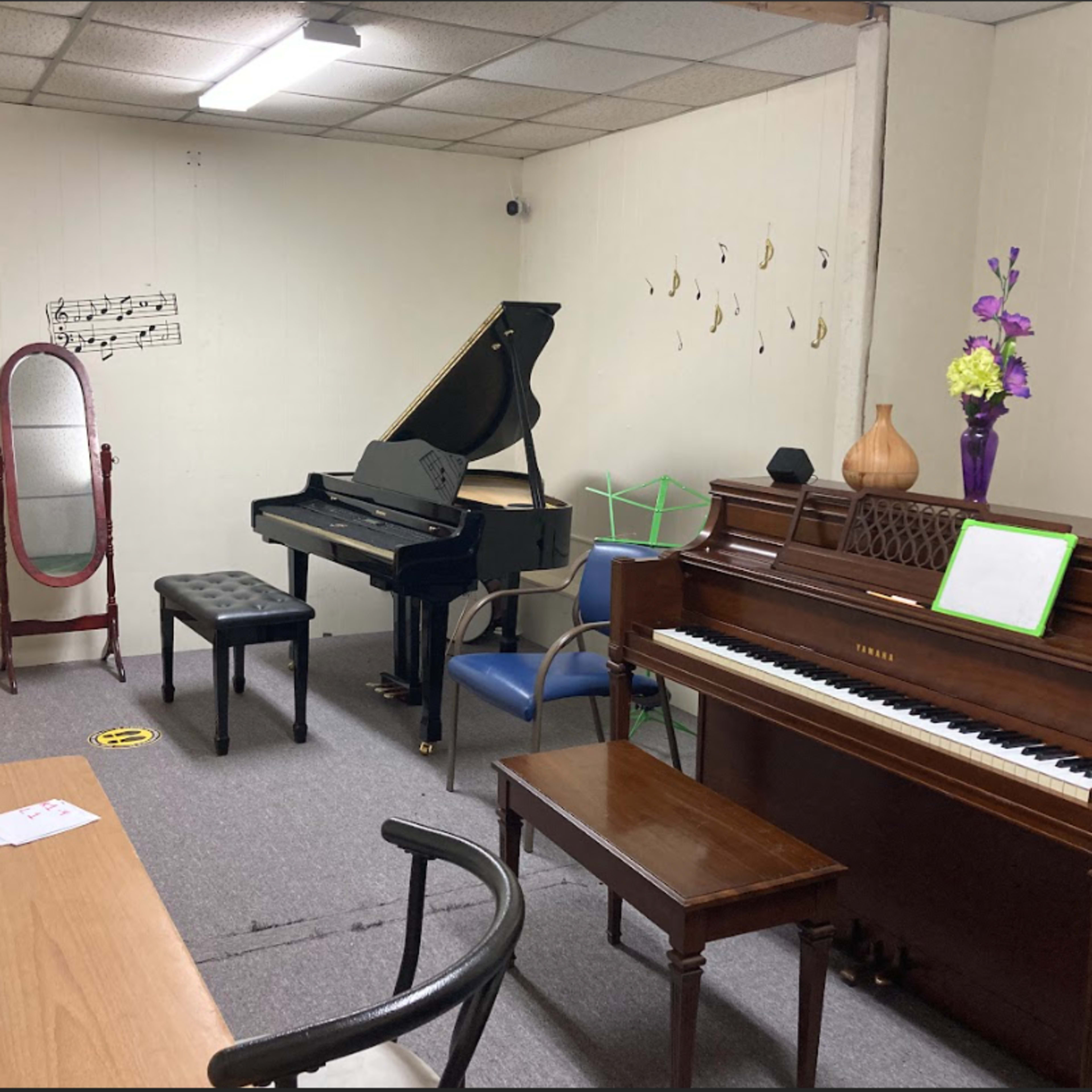 The room contains two pianos, a mirrored stand, a music stand, a table, and decorative elements, all arranged with musical notes on the walls.