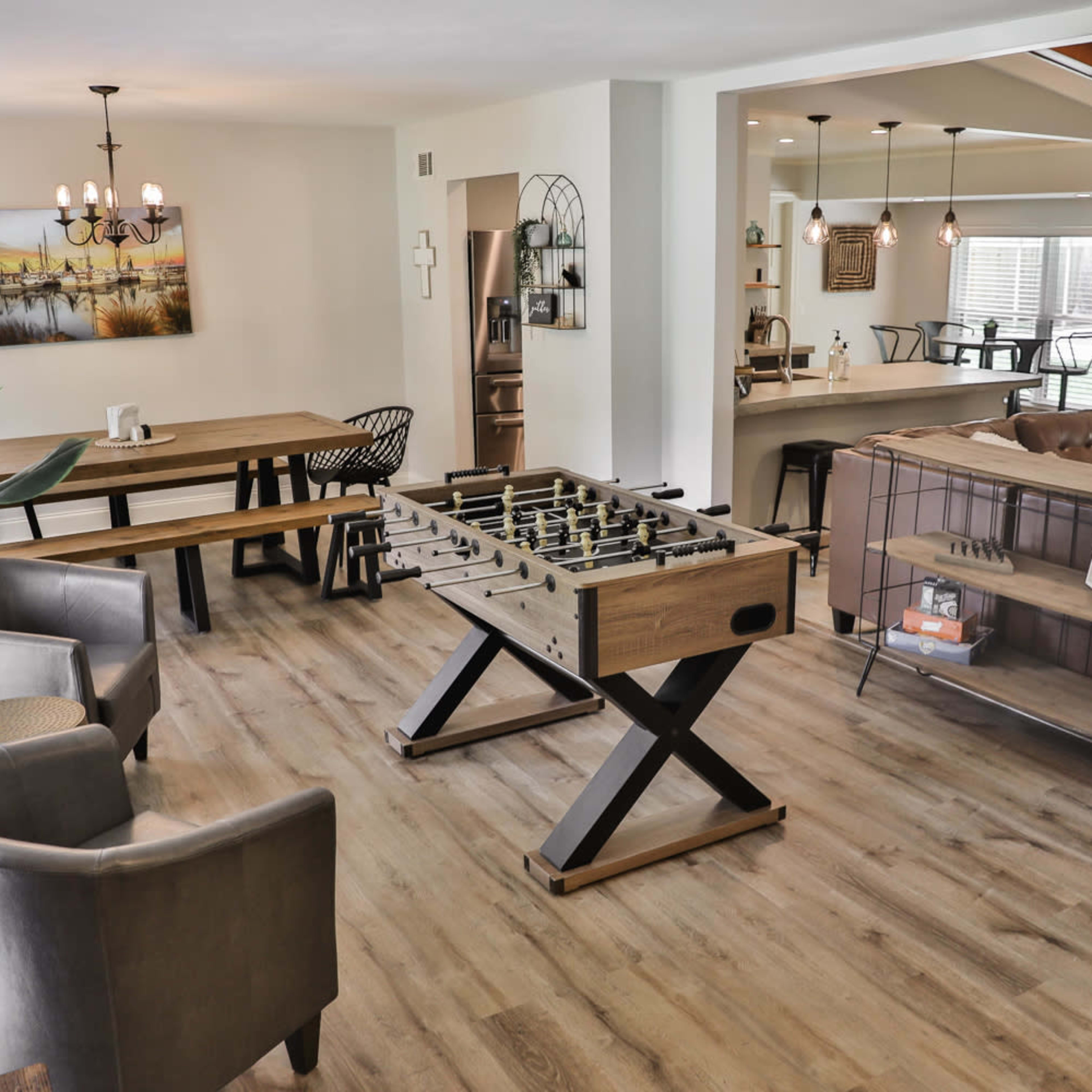 A spacious indoor area with a foosball table, a wooden dining table, two chairs, and a living room visible in the background.