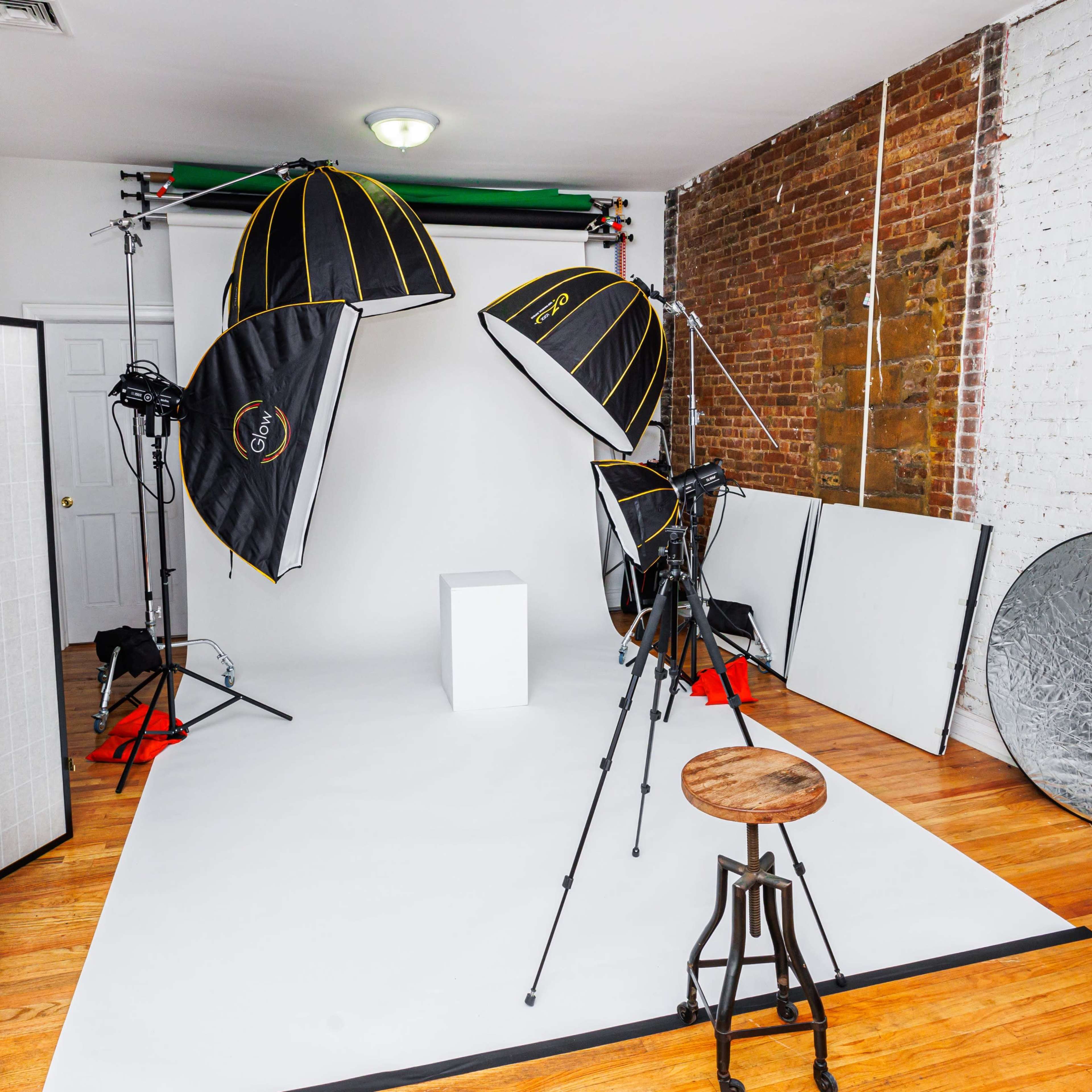 A photography studio setup with multiple lighting fixtures, a backdrop, and props arranged on a wooden floor.