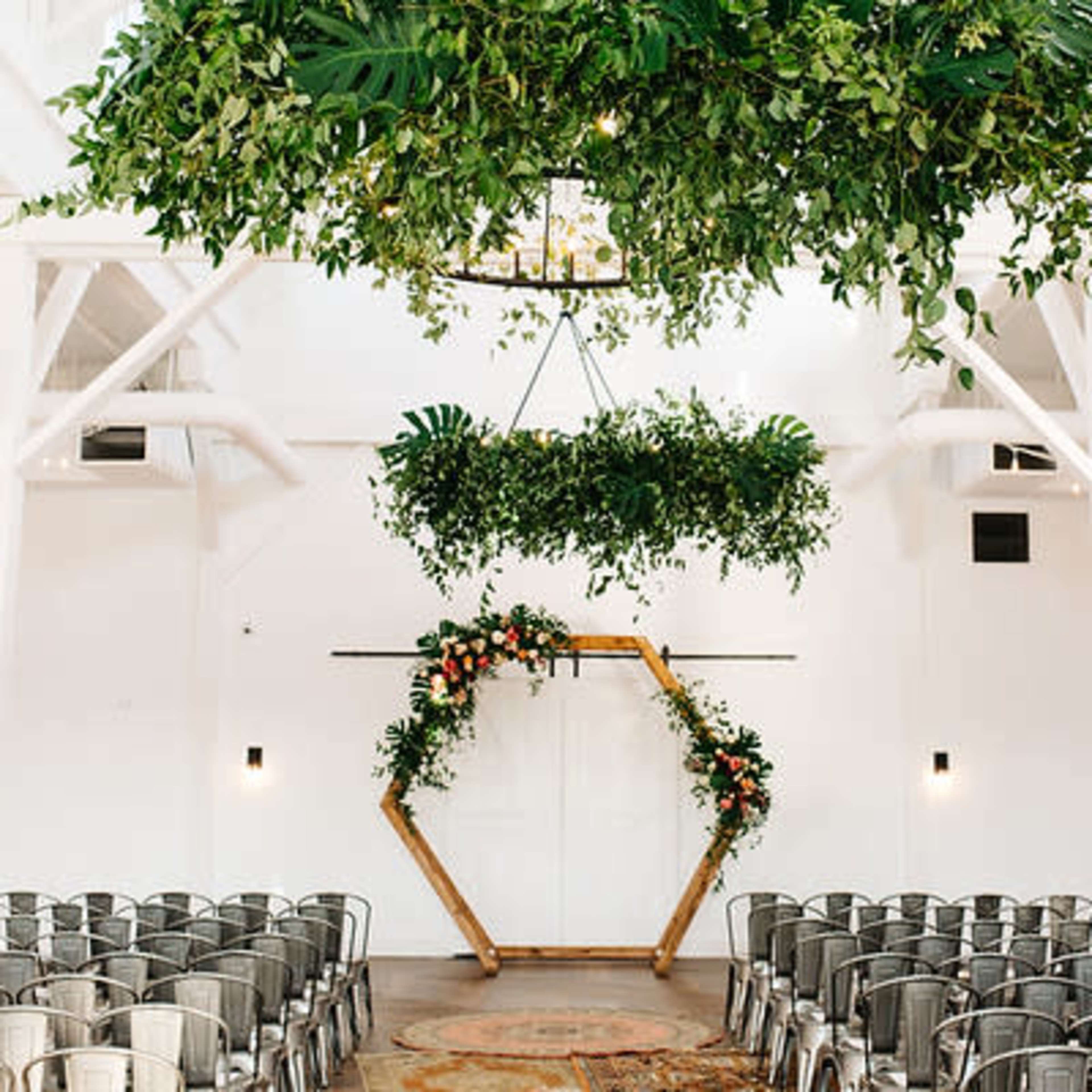 A wedding ceremony space with an arch decorated with greenery and floral arrangements, surrounded by rows of metal chairs.
