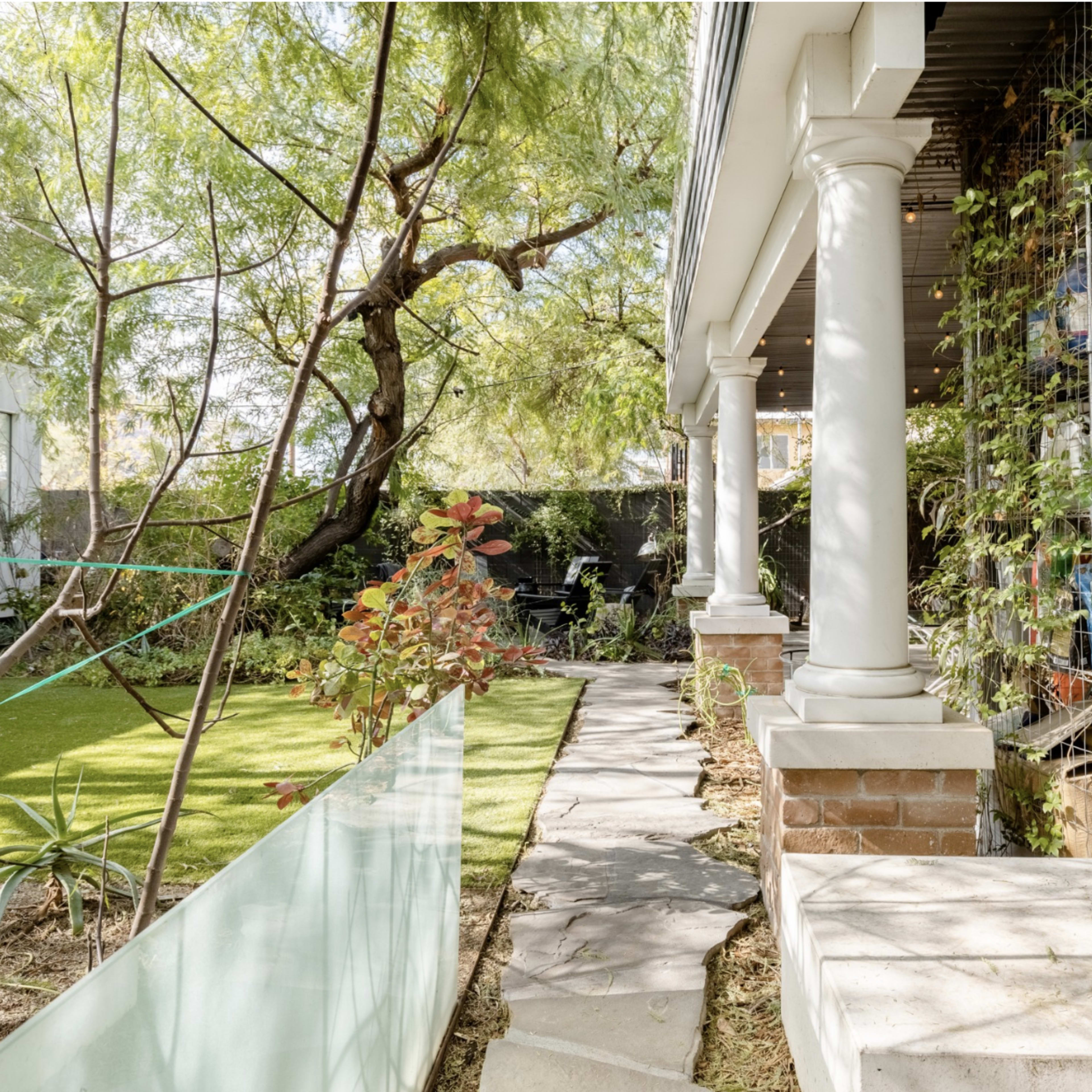 A landscaped garden area with a stone pathway, modern columns, and greenery surrounding a building structure.