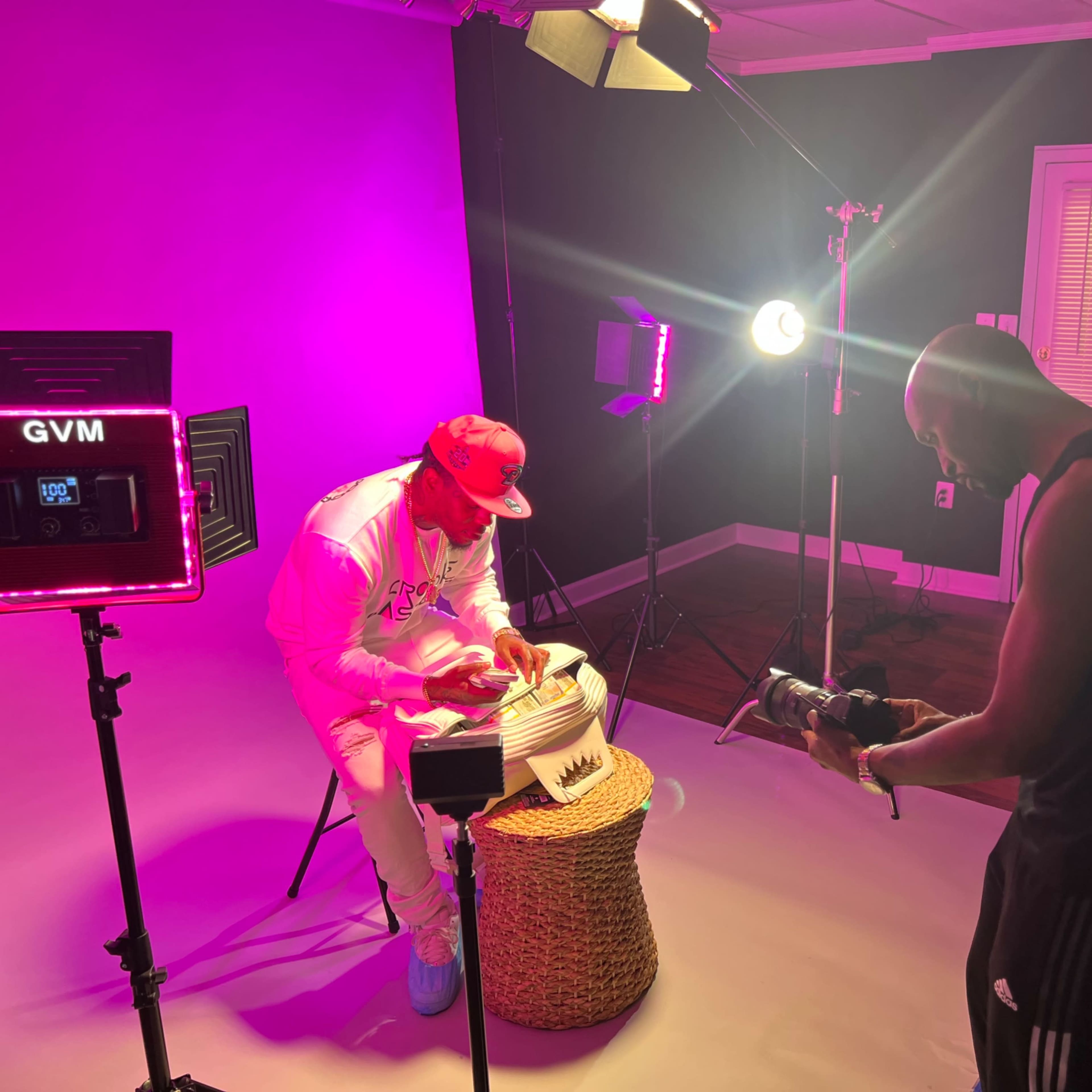 A photographer captures a subject sitting on a stool in a brightly lit studio with pink lighting.