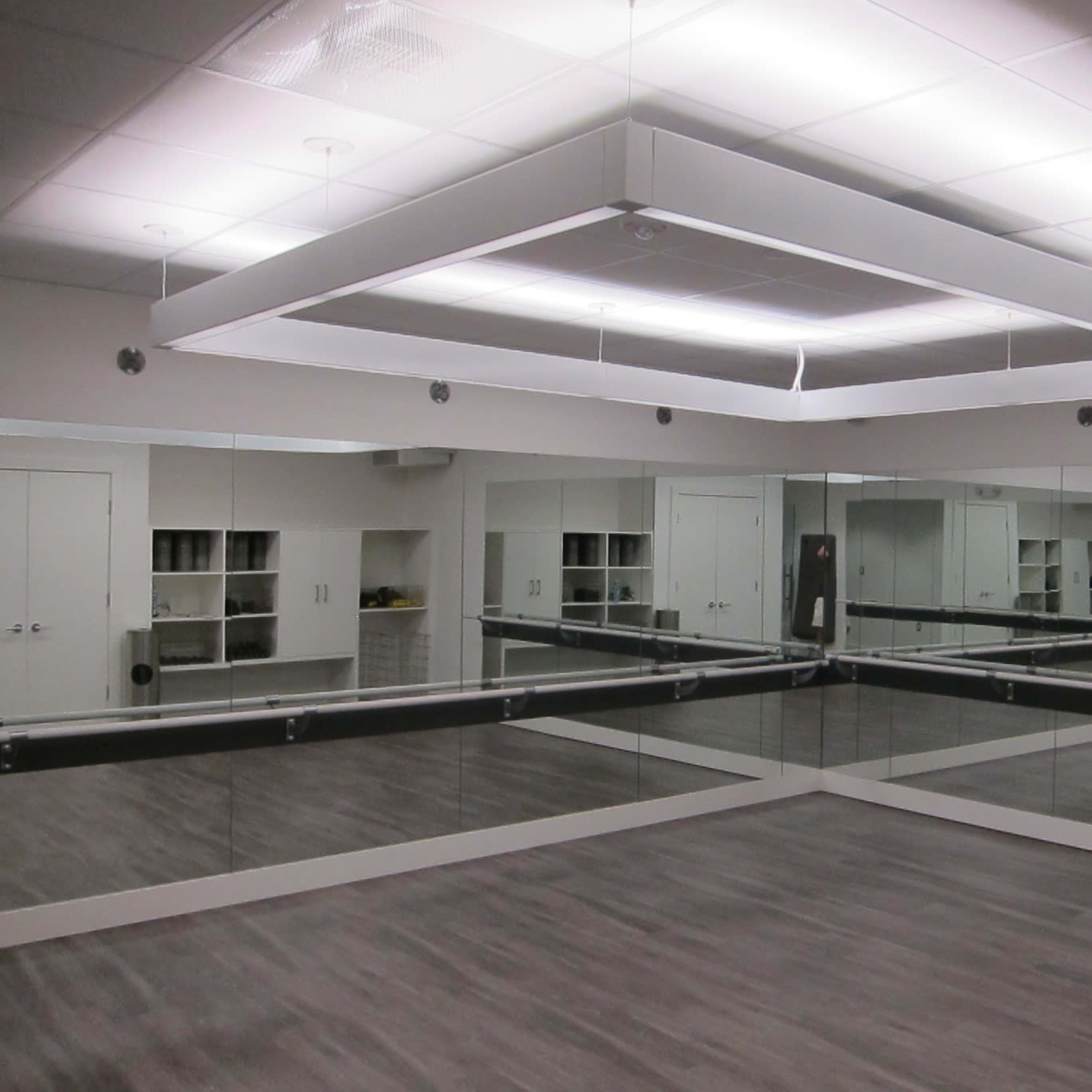 A mirrored dance studio with sleek wooden flooring and overhead lighting.