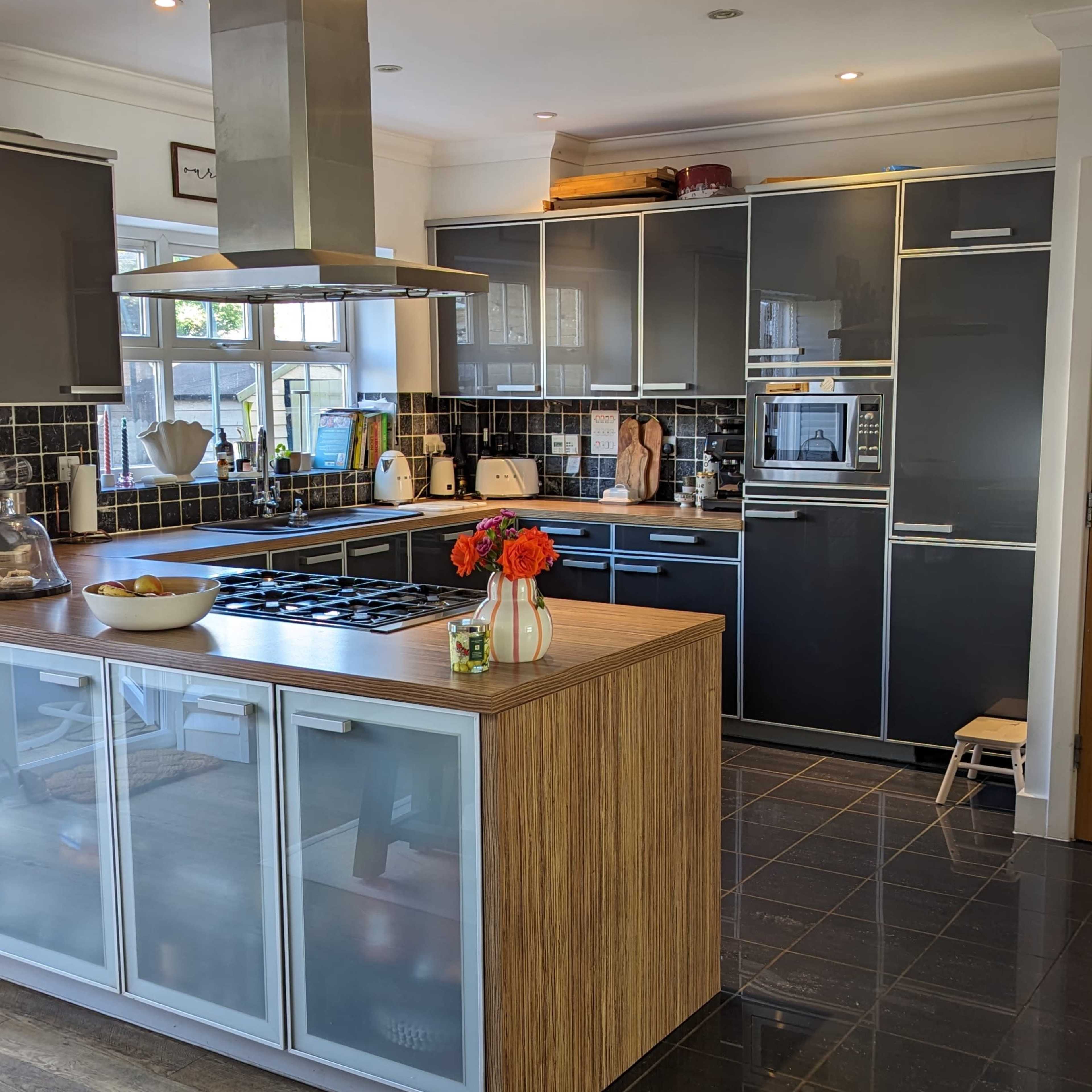 A modern kitchen with dark cabinets, a large island with a stovetop, and a tiled floor.
