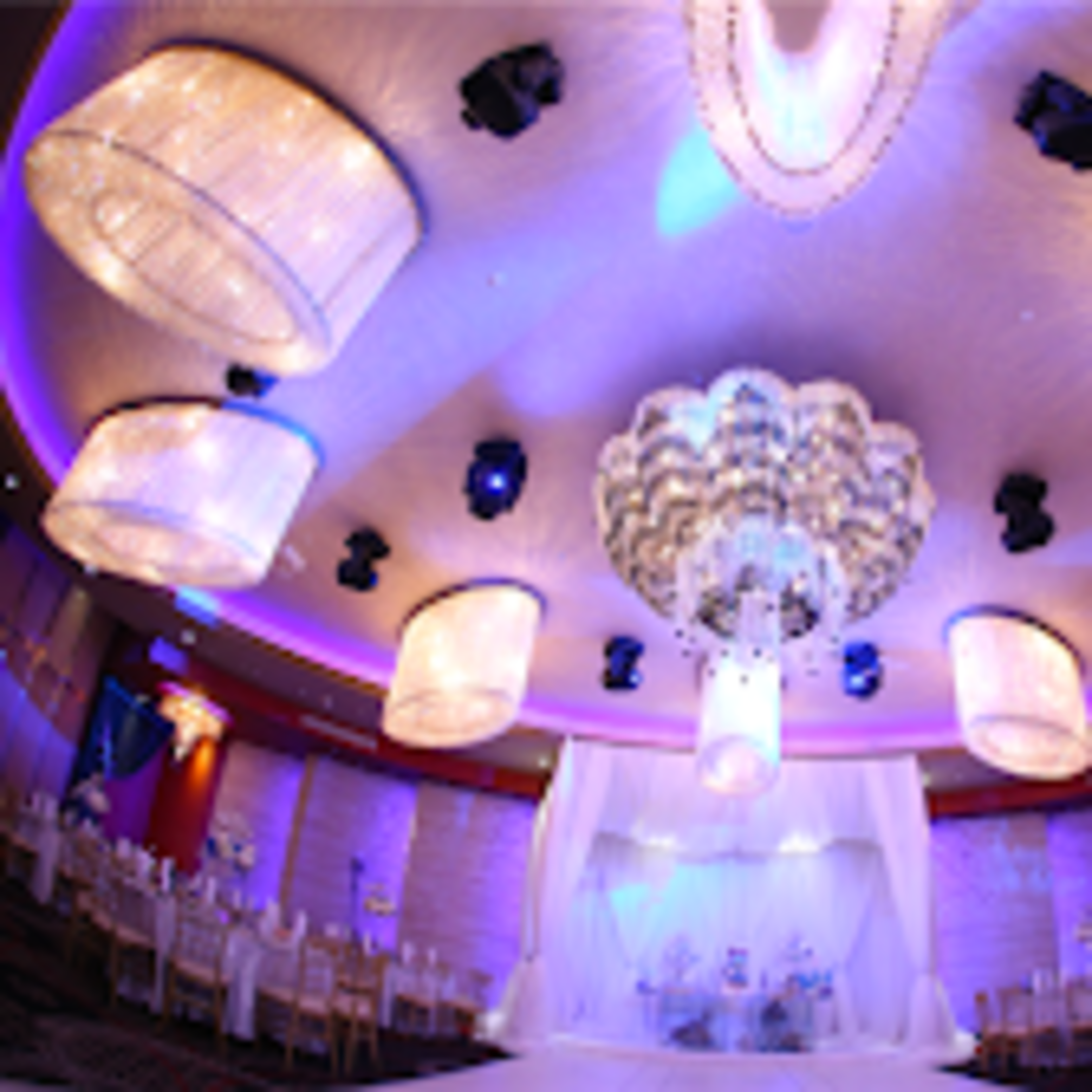 An elegantly decorated indoor venue with a large chandelier, suspended lights, and rows of chairs arranged for a wedding ceremony.