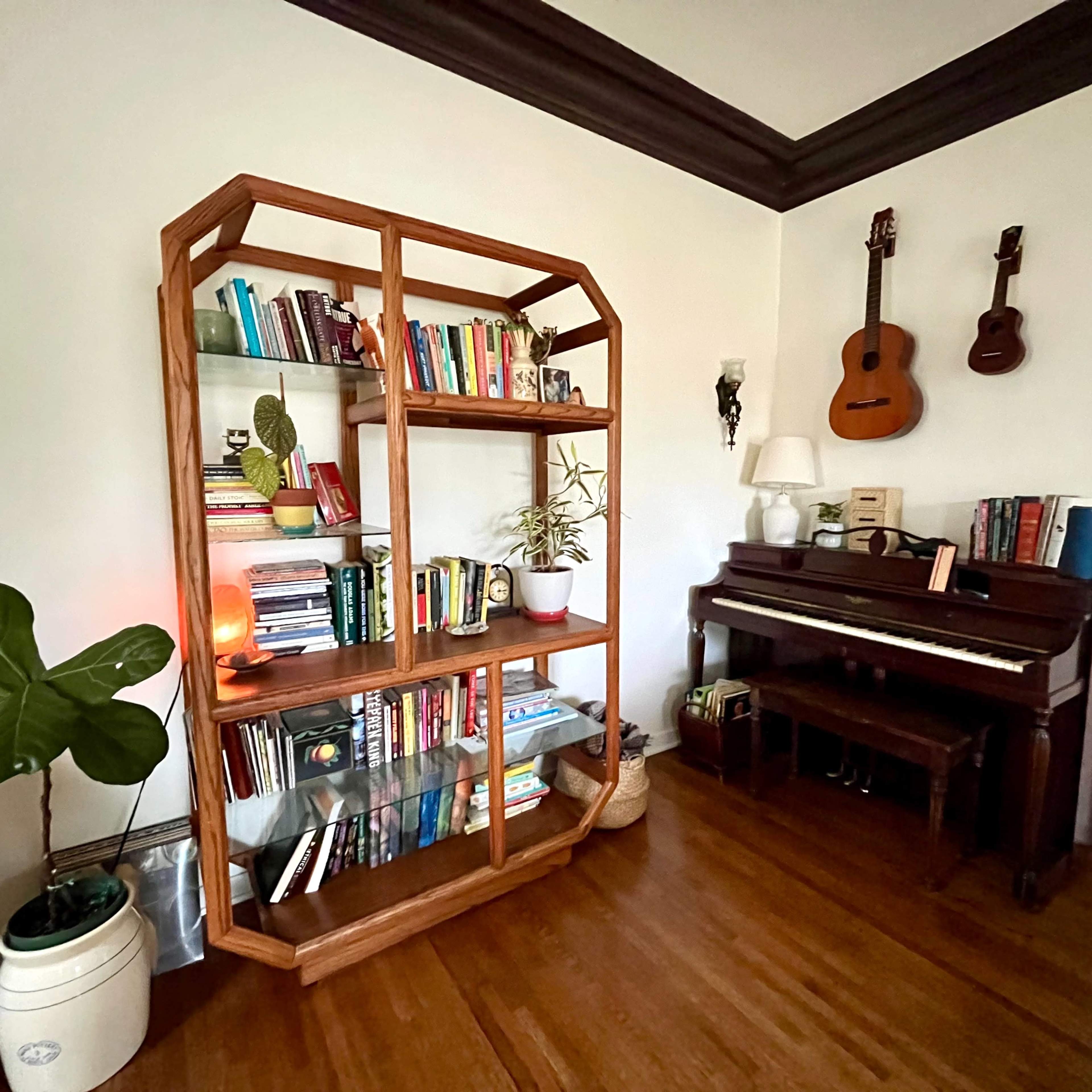 A cozy room featuring a wooden bookshelf filled with books, a piano, and a couple of guitars hanging on the wall.