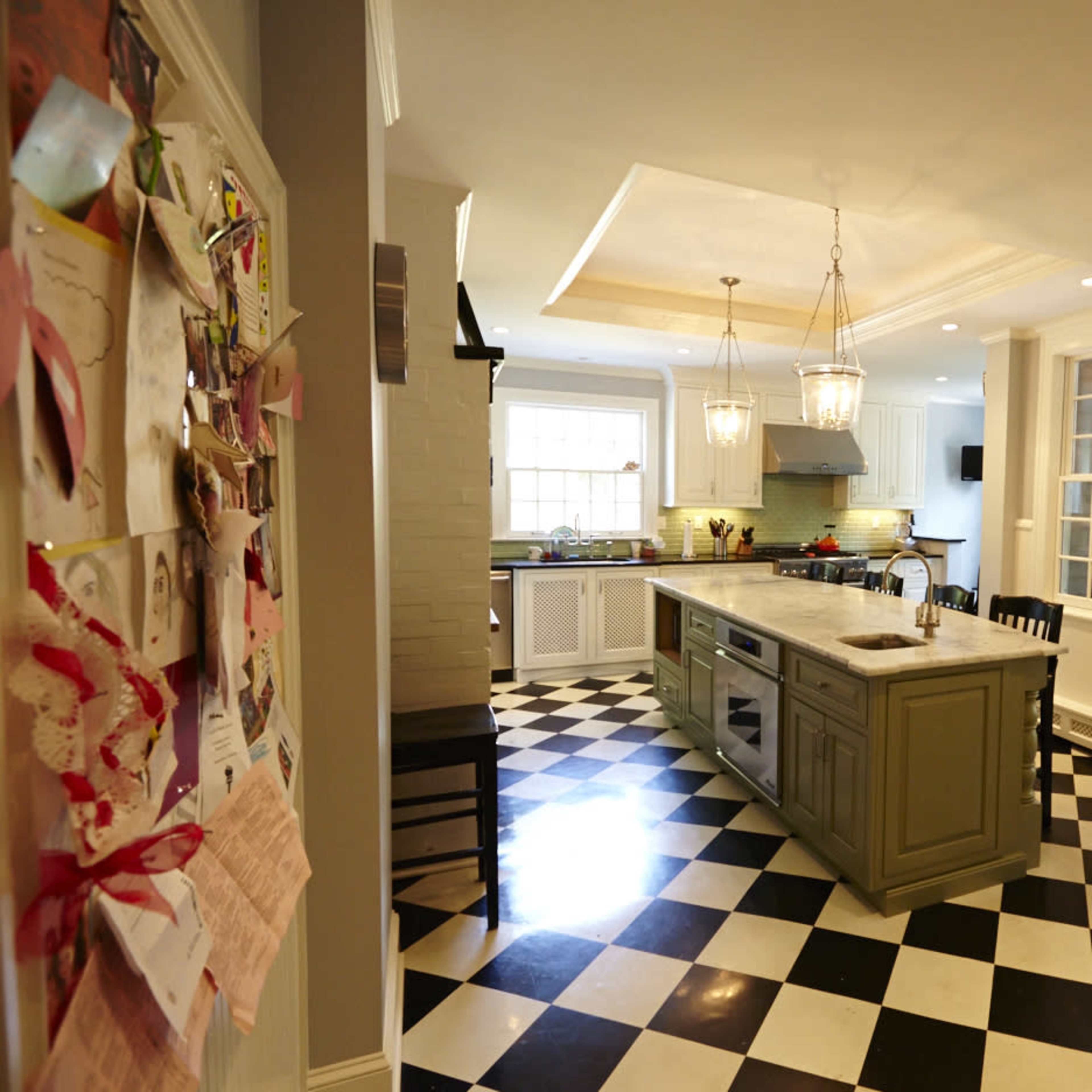 The kitchen features a checkered black and white floor, a central island, and pendant lighting above a spacious countertop.