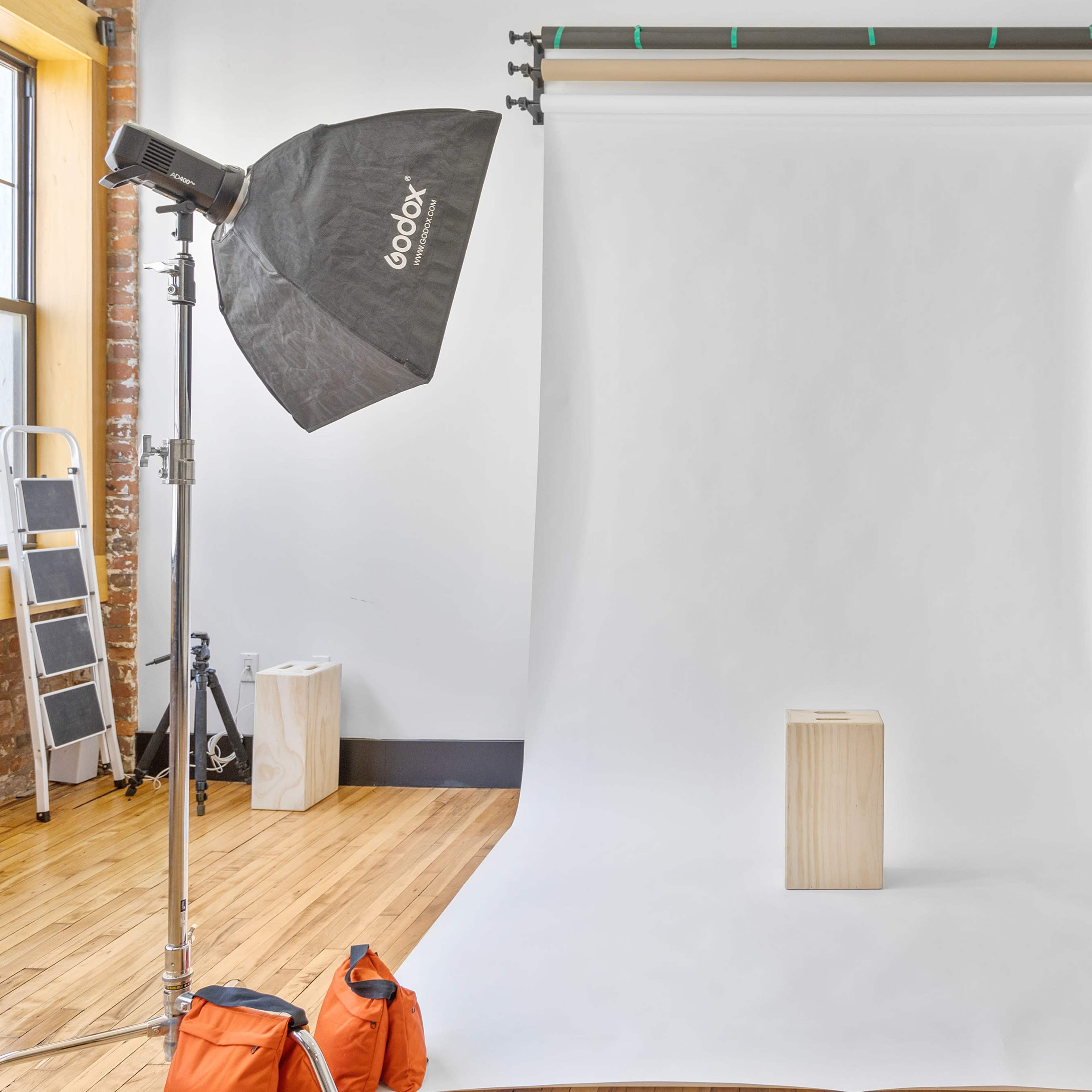 A photography studio setup with a white backdrop, a wooden pedestal in the center, and lighting equipment on either side.