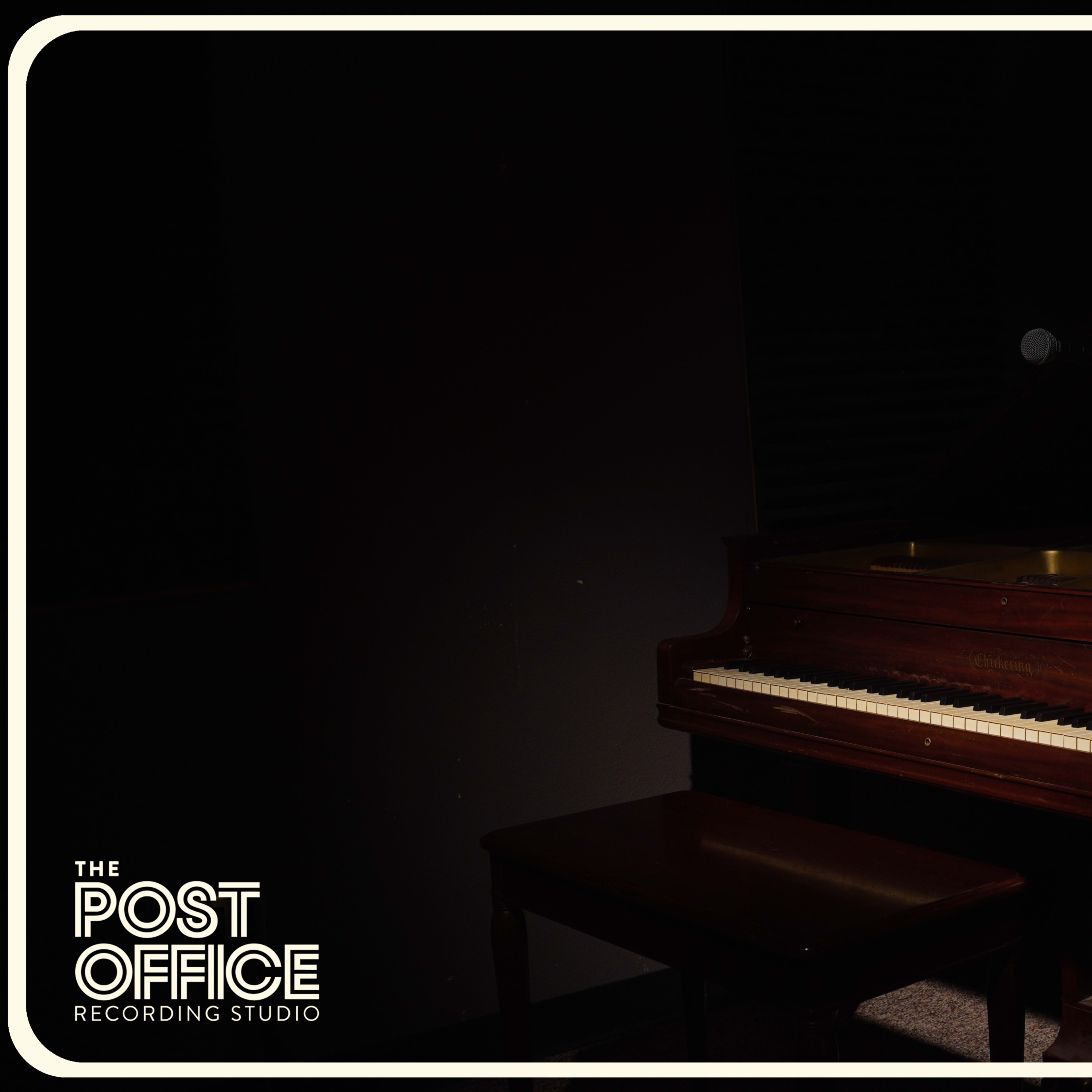 A grand piano and a microphone are positioned in a dimly lit recording studio.