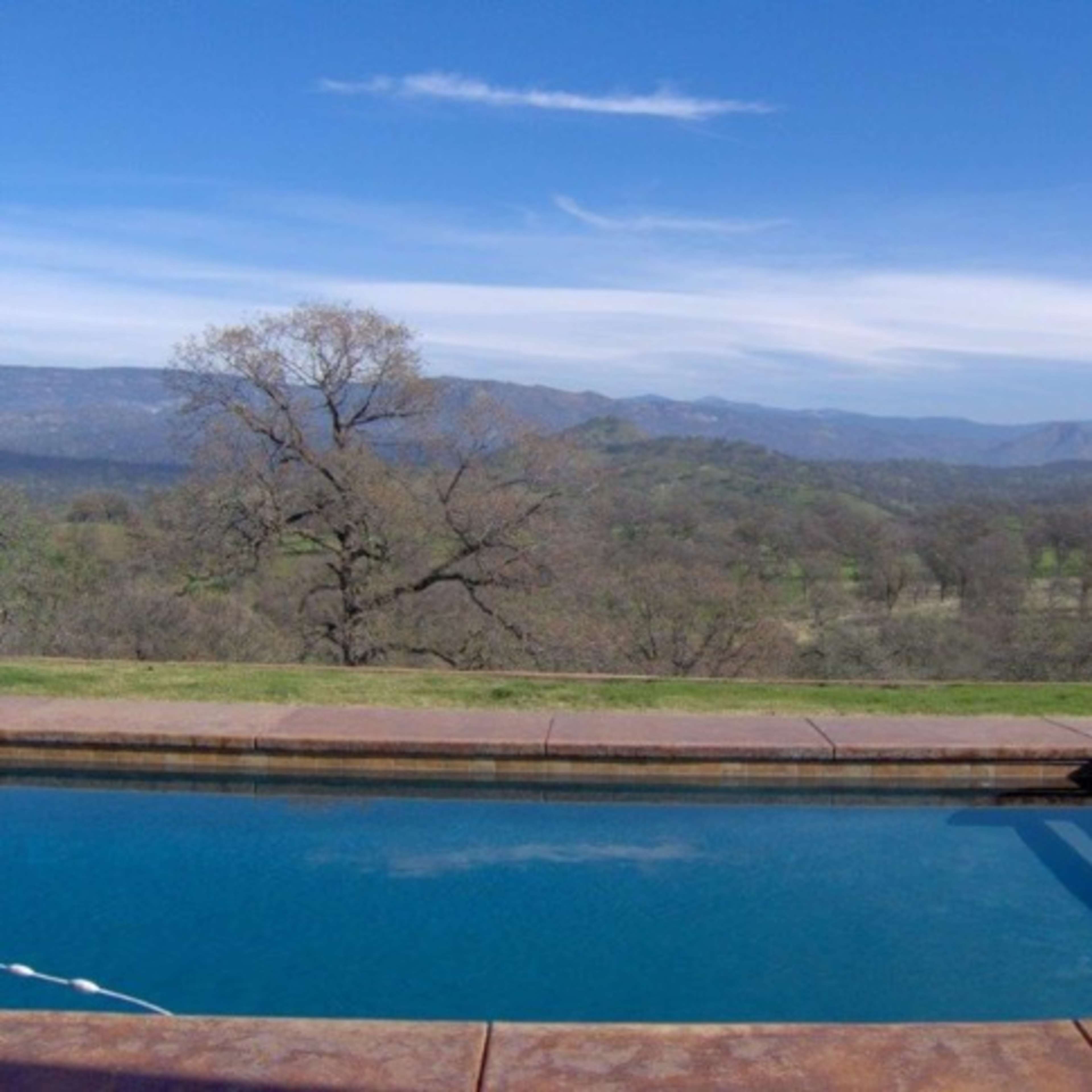 A clear blue swimming pool with a mountainous landscape in the background under a partly cloudy sky.
