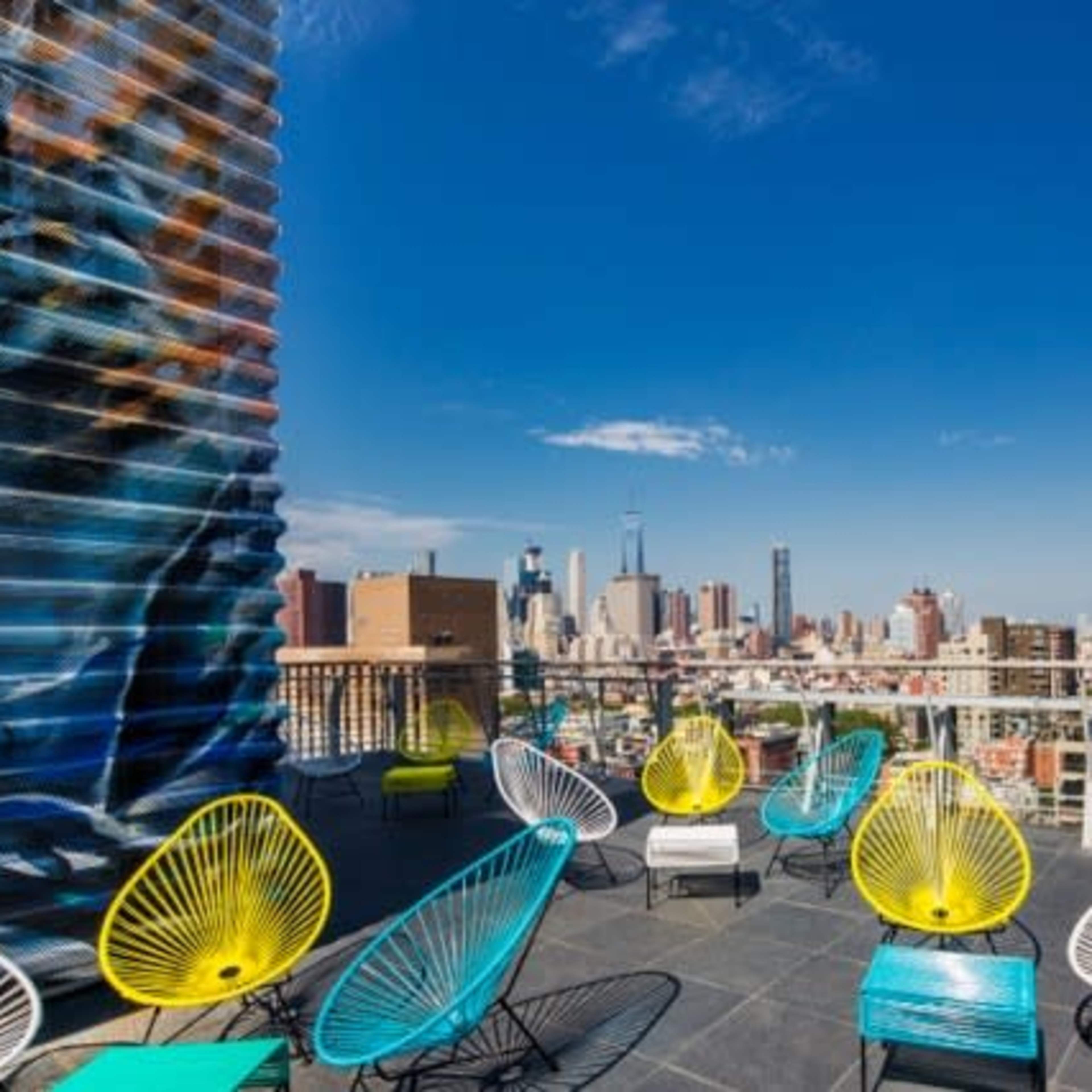 A rooftop terrace with colorful chairs overlooking a city skyline under a clear blue sky.