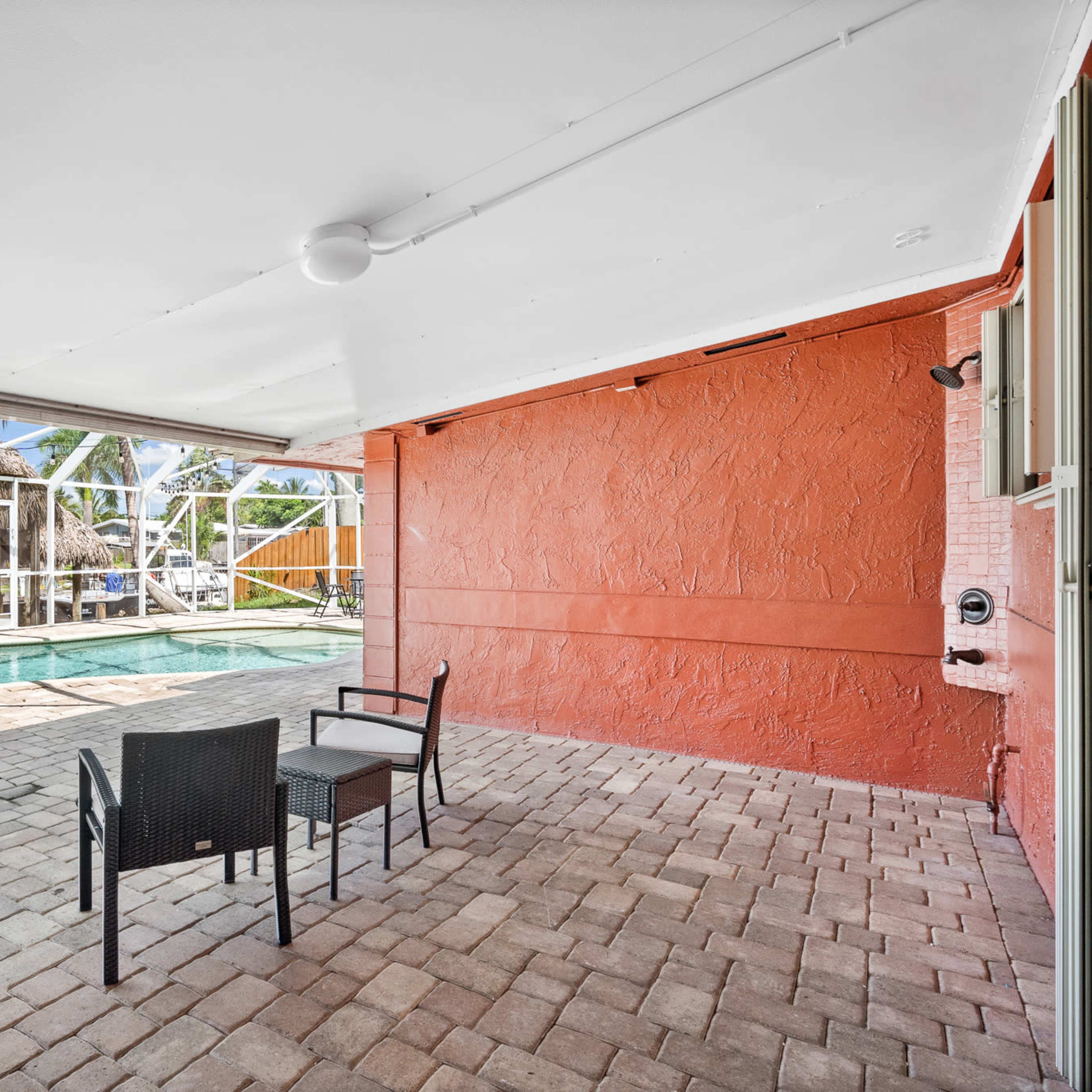 A covered patio area with two chairs overlooking a swimming pool surrounded by a screened enclosure.