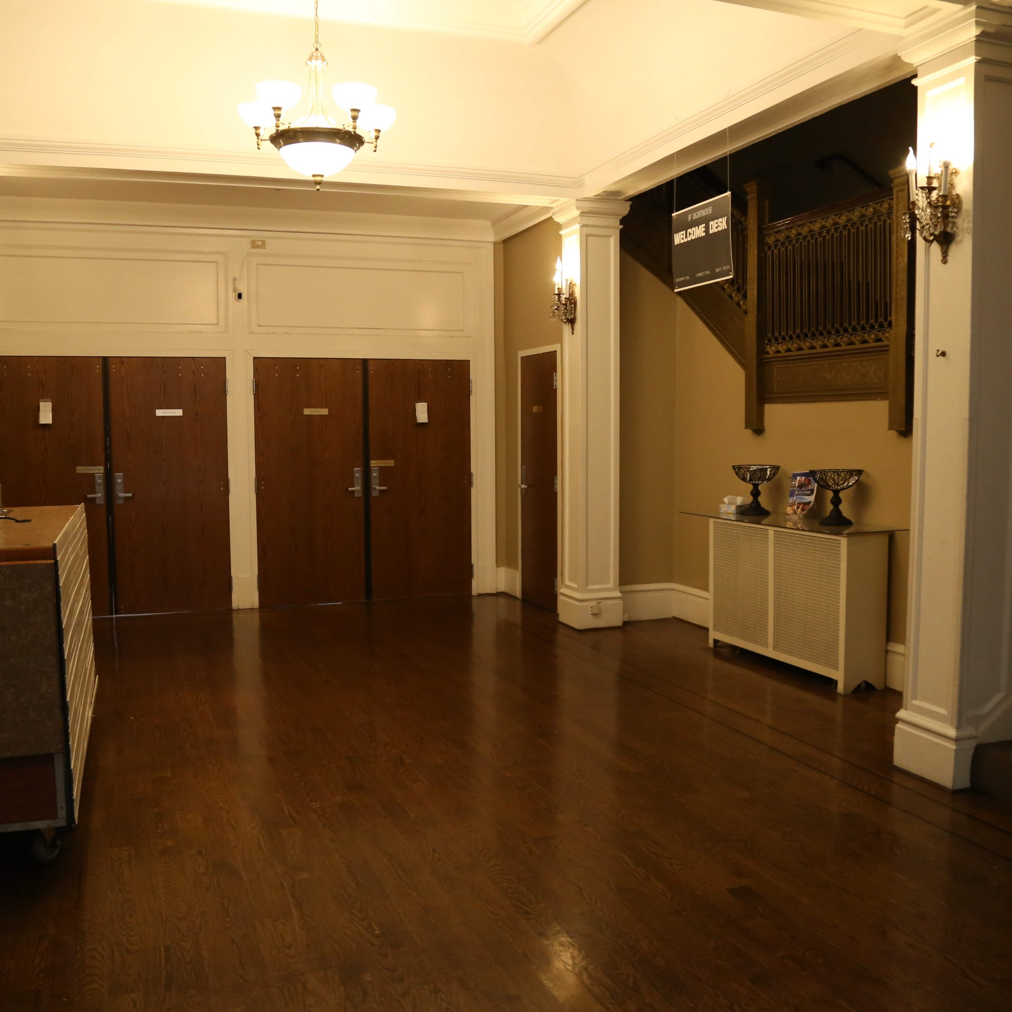 A spacious lobby with a reception desk, two wooden double doors, and a staircase leading to an upper level.