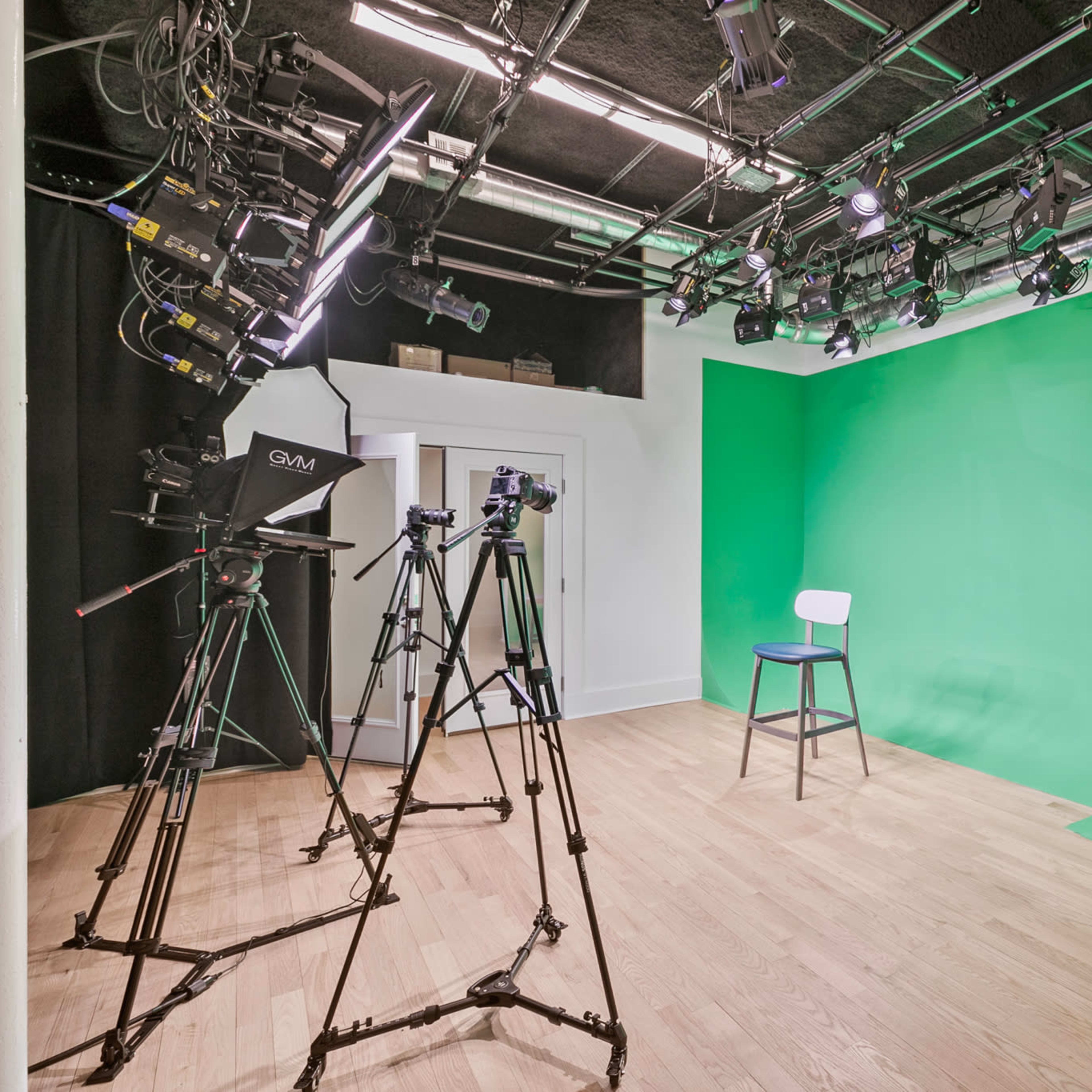 A studio with a green screen backdrop, a chair, and three cameras positioned on tripods.