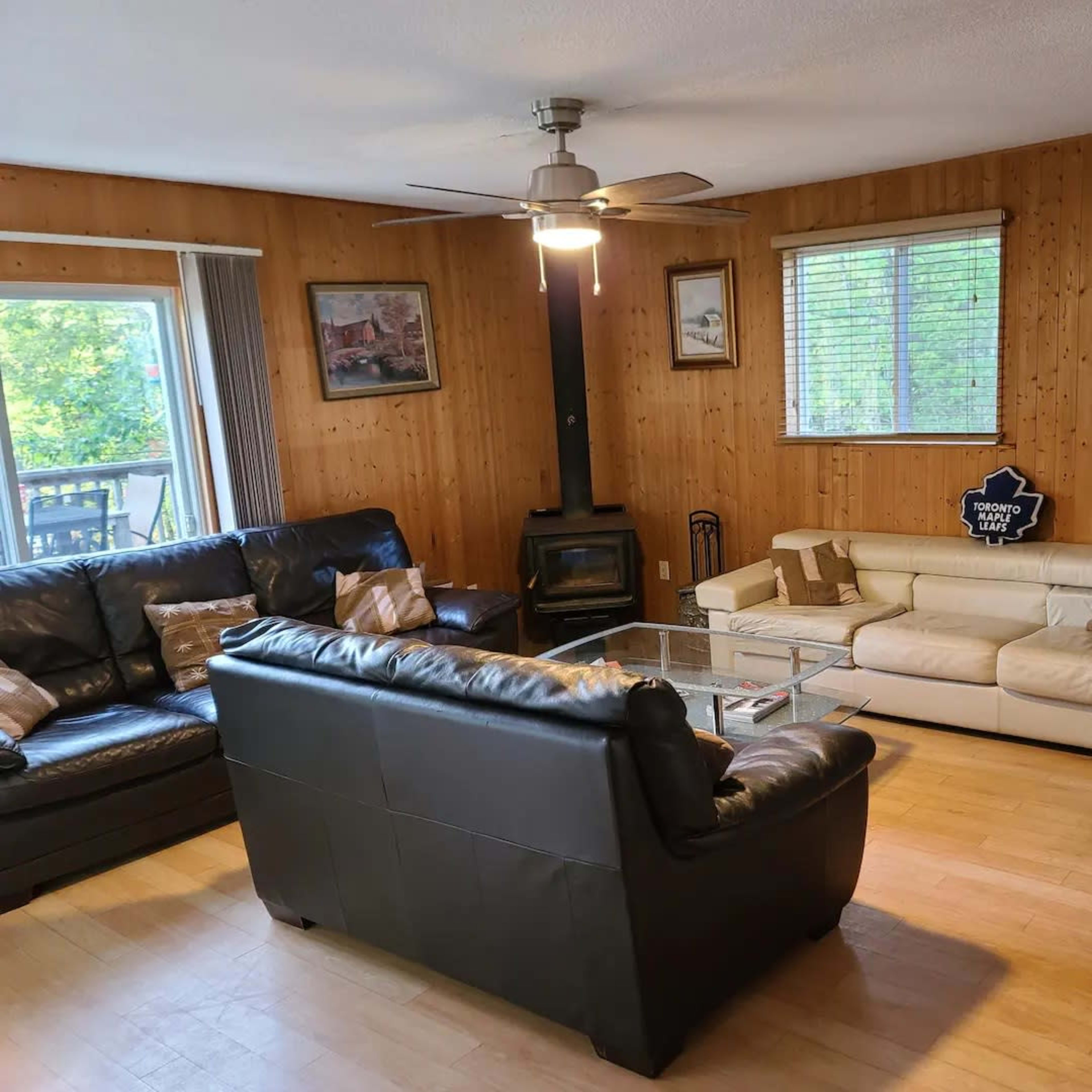 A living room with wooden paneling, two sofas, a glass coffee table, and a window letting in natural light.