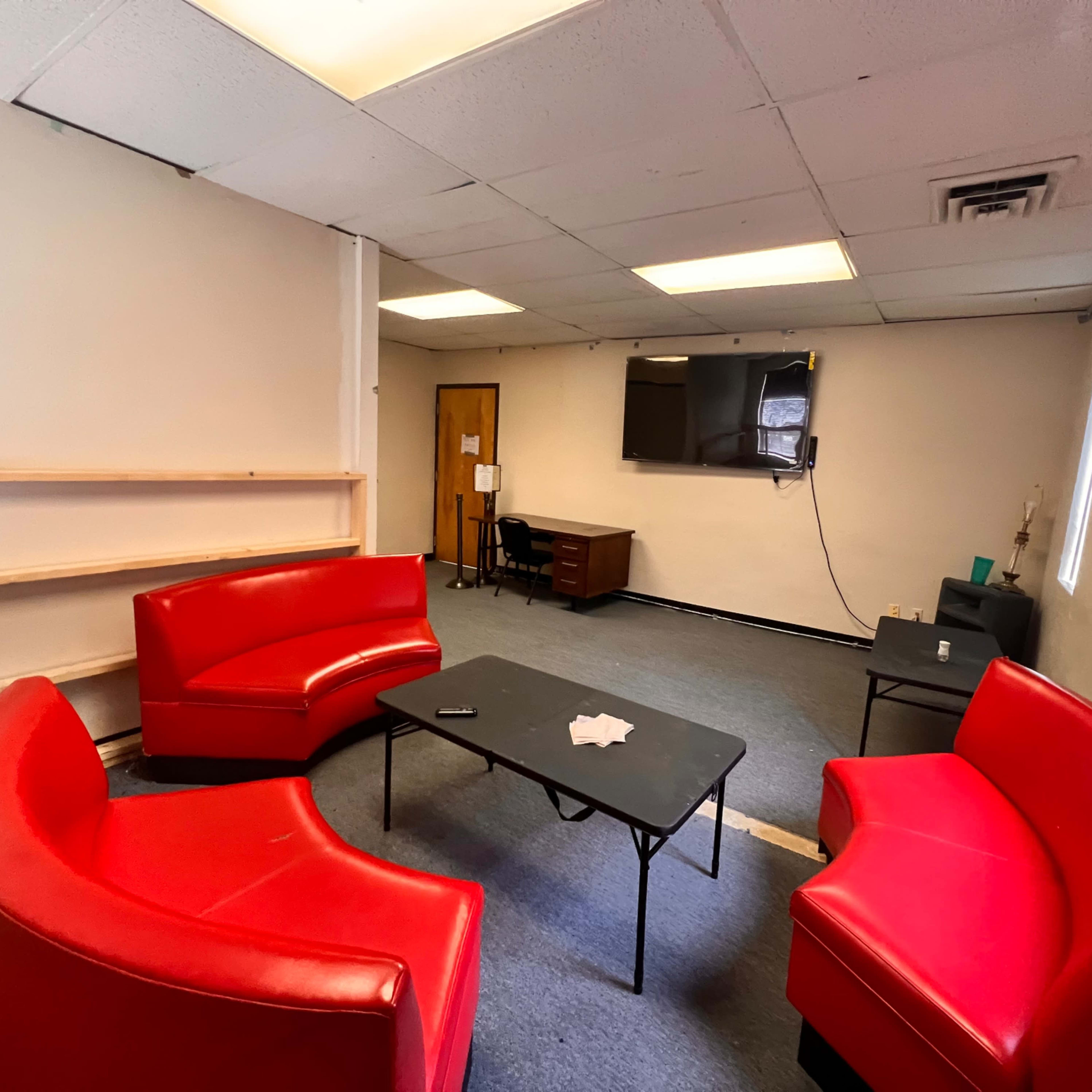 A sparsely furnished room with two red curved sofas, a black table in the center, and a desk with a television mounted on the wall.