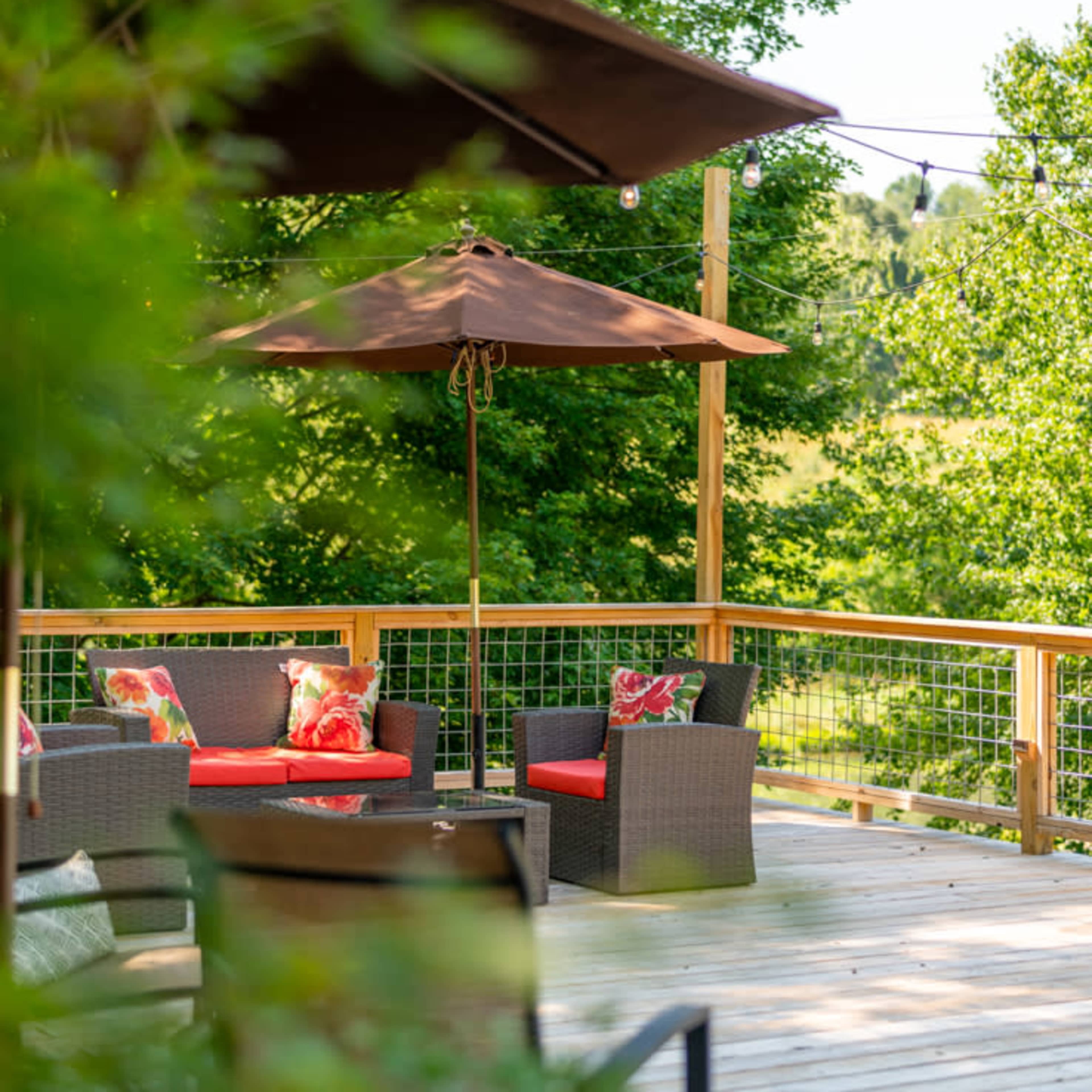 A wooden deck is surrounded by greenery and features outdoor seating with umbrellas.