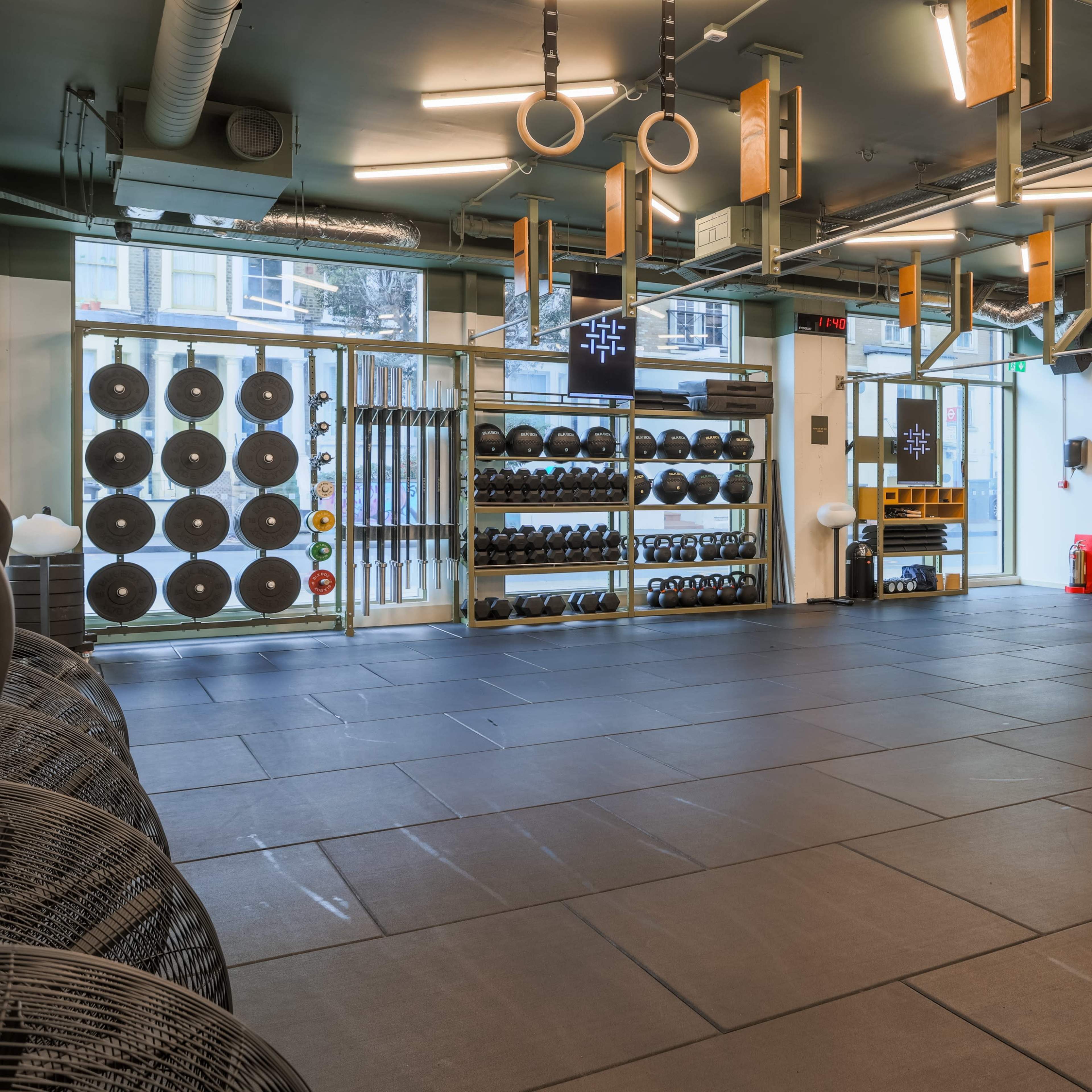 A fitness studio equipped with various gym weights, resistance bands, and gymnastic rings, with an open layout and large windows.