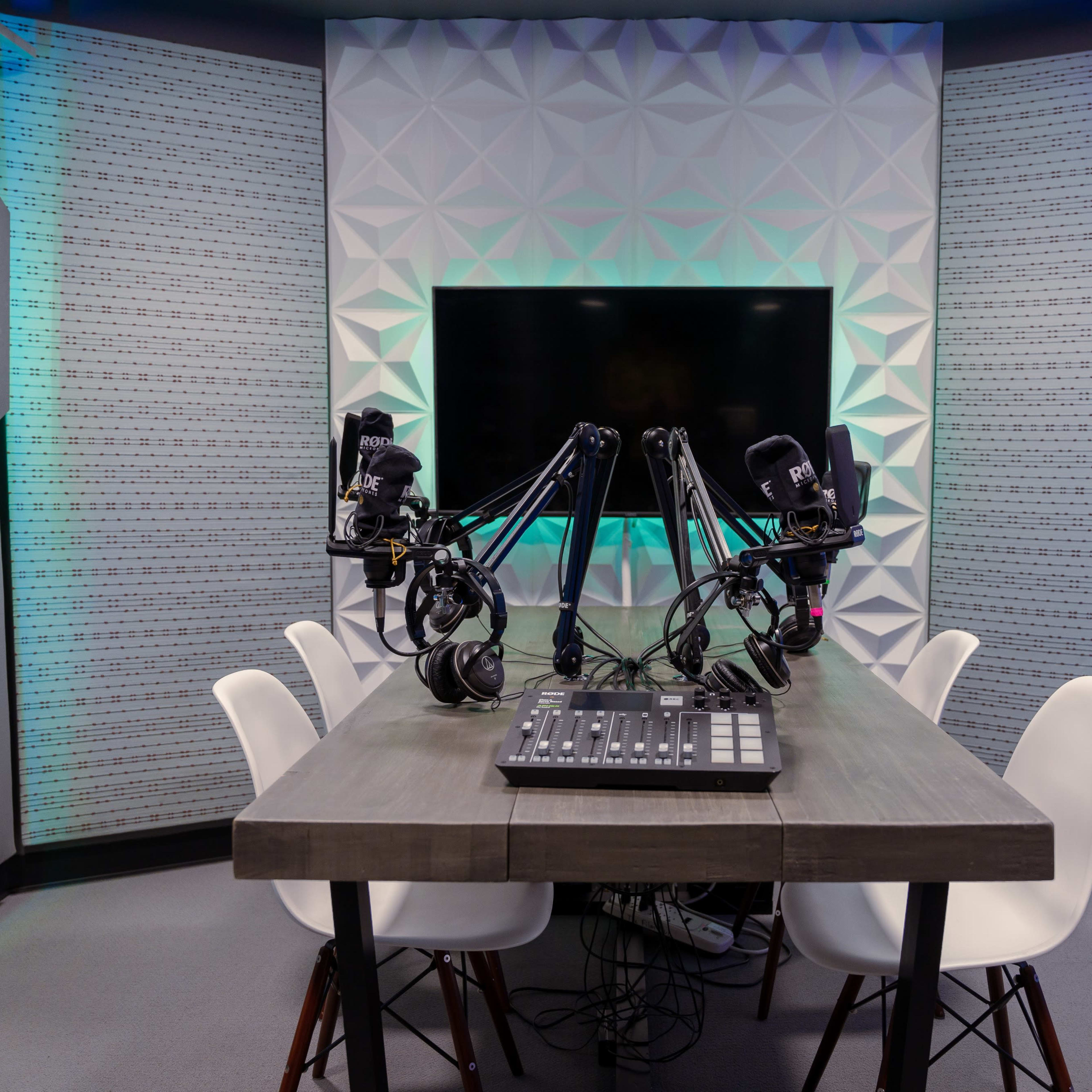A podcast recording studio equipped with a table, four chairs, and two mounted microphones.