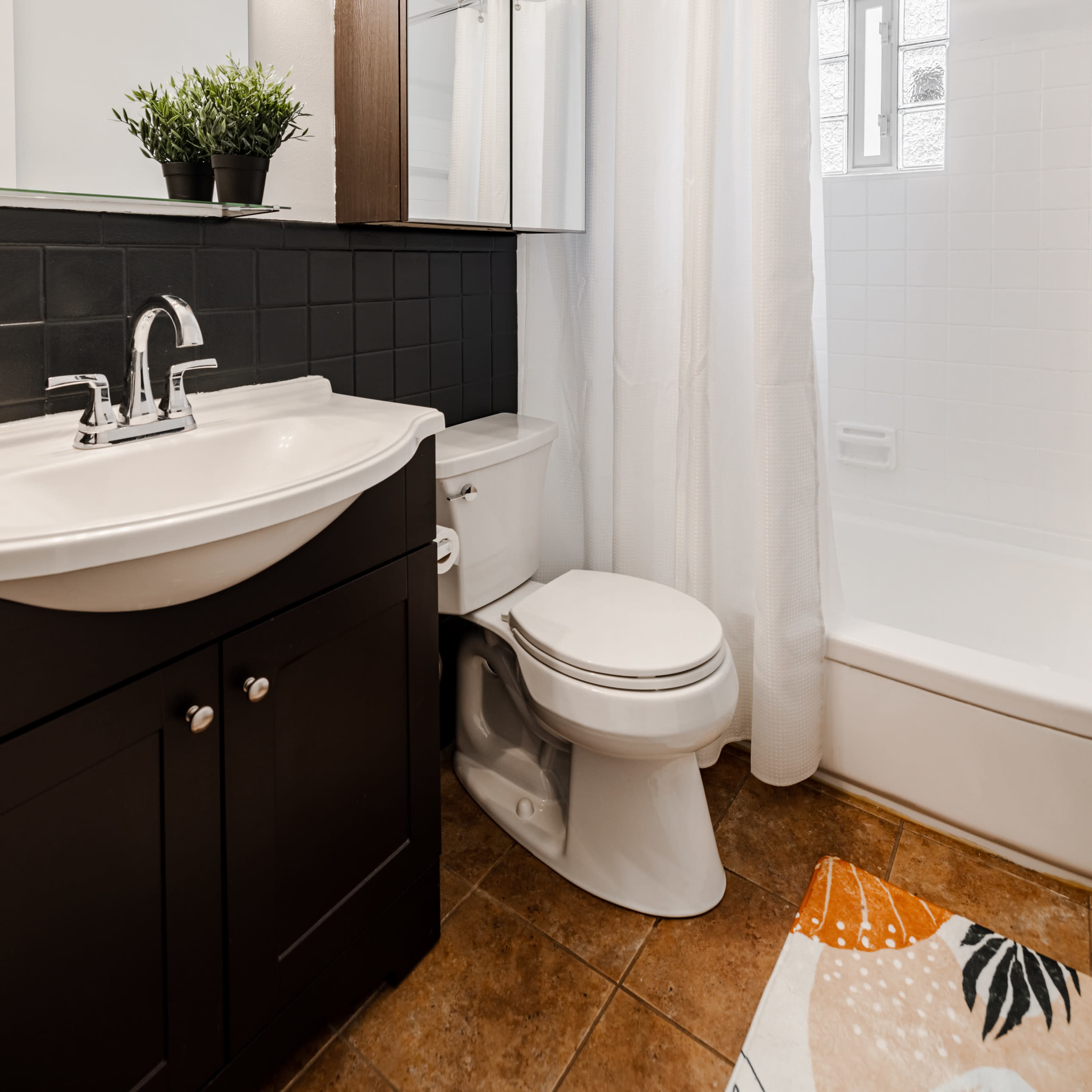 A modern bathroom featuring a white shower curtain, a sleek black vanity with a sink, a toilet, and a bathtub.