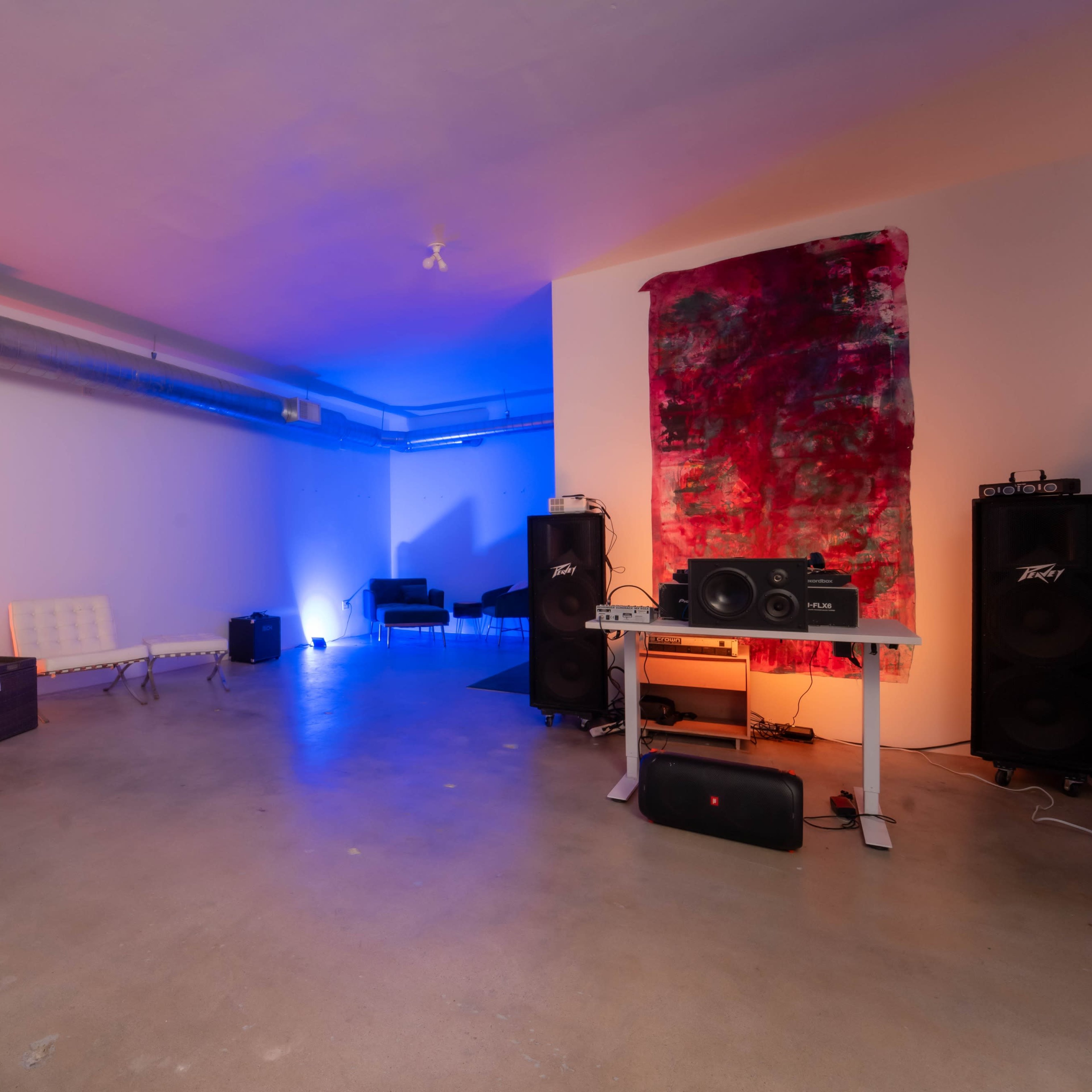 A spacious room features minimalist white furniture, colorful lighting, and audio equipment set up for a music setting.