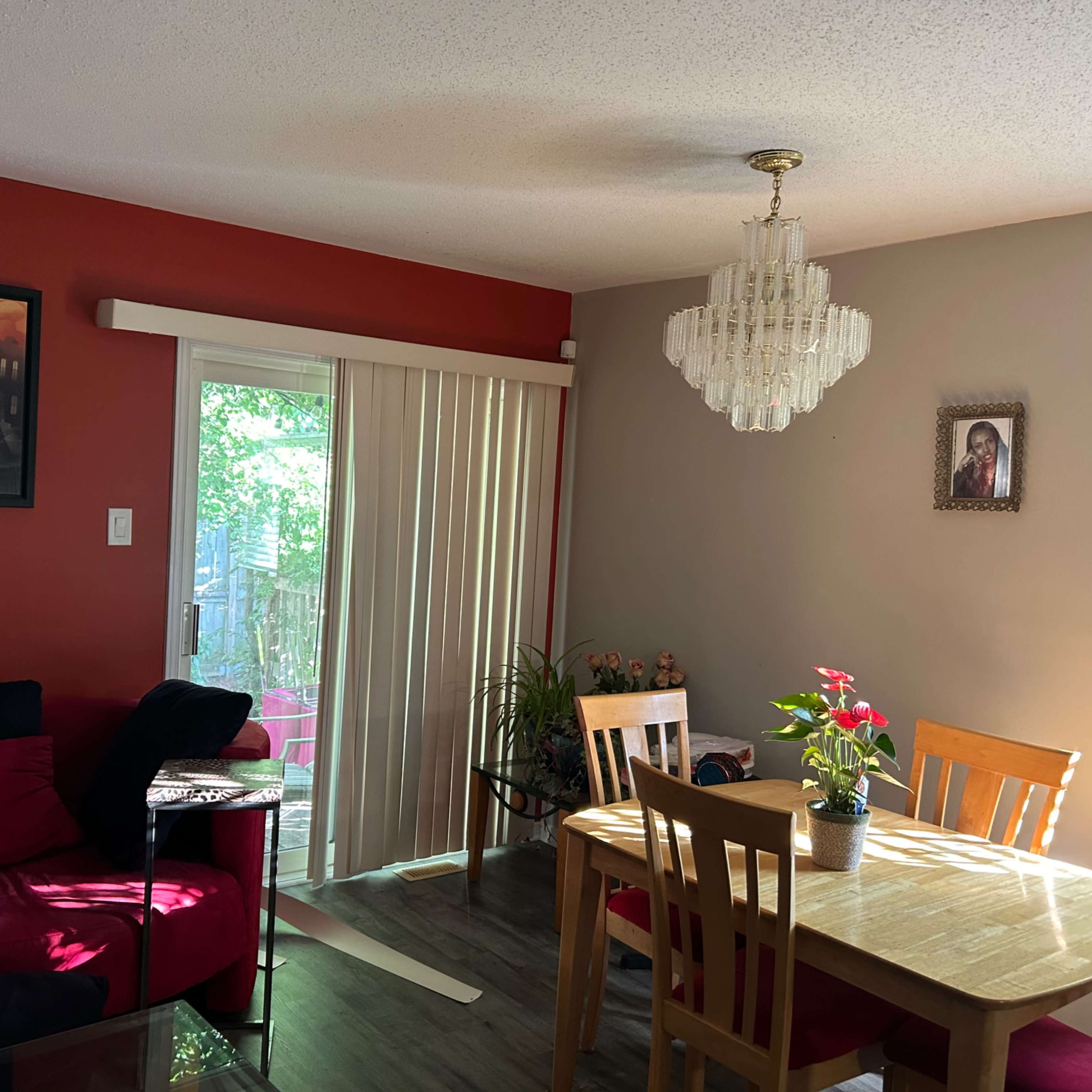 A living room with a red accent wall, a dining table, sliding glass doors, and artwork on the walls.