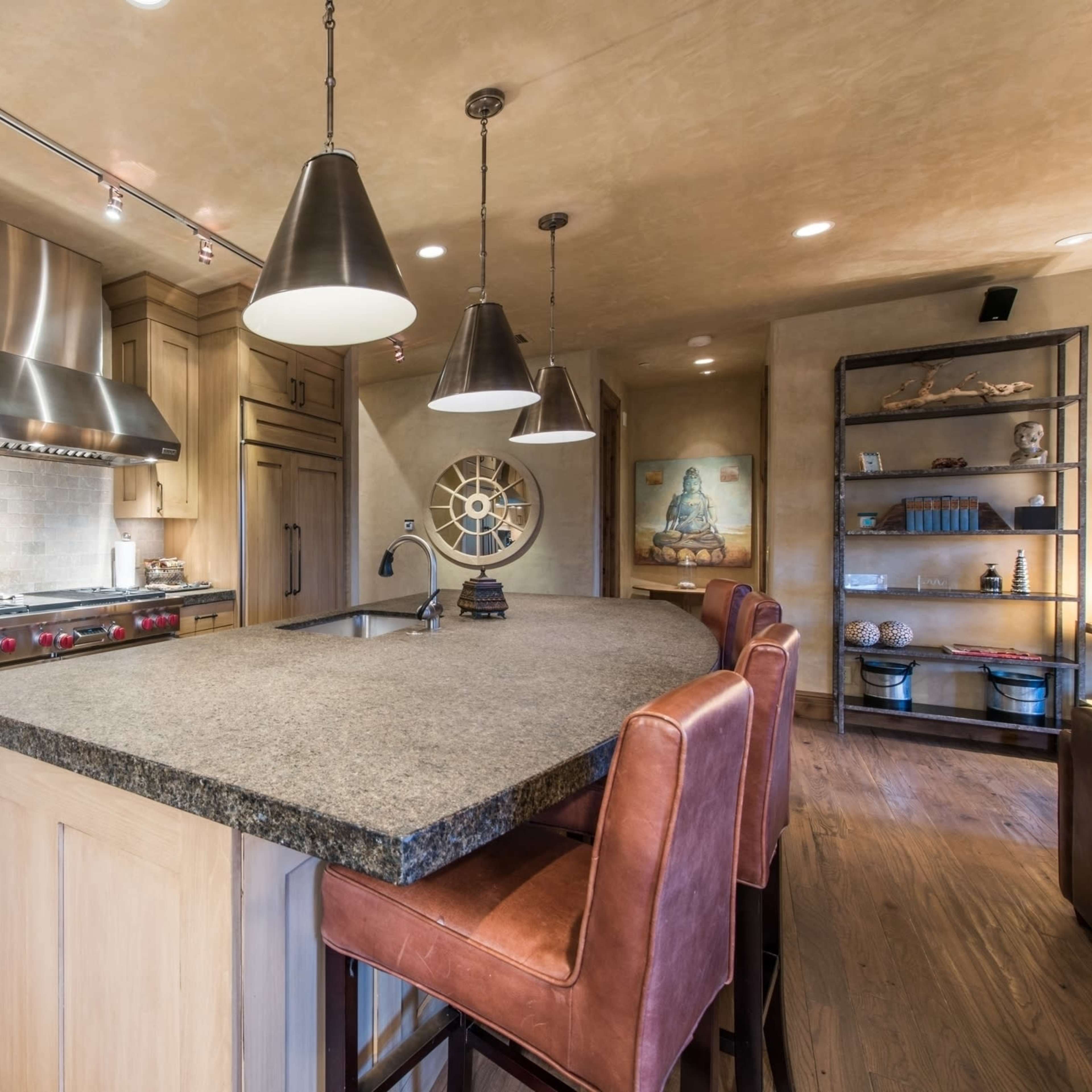 A modern kitchen with wooden cabinets, a large island with bar stools, and stainless steel appliances.