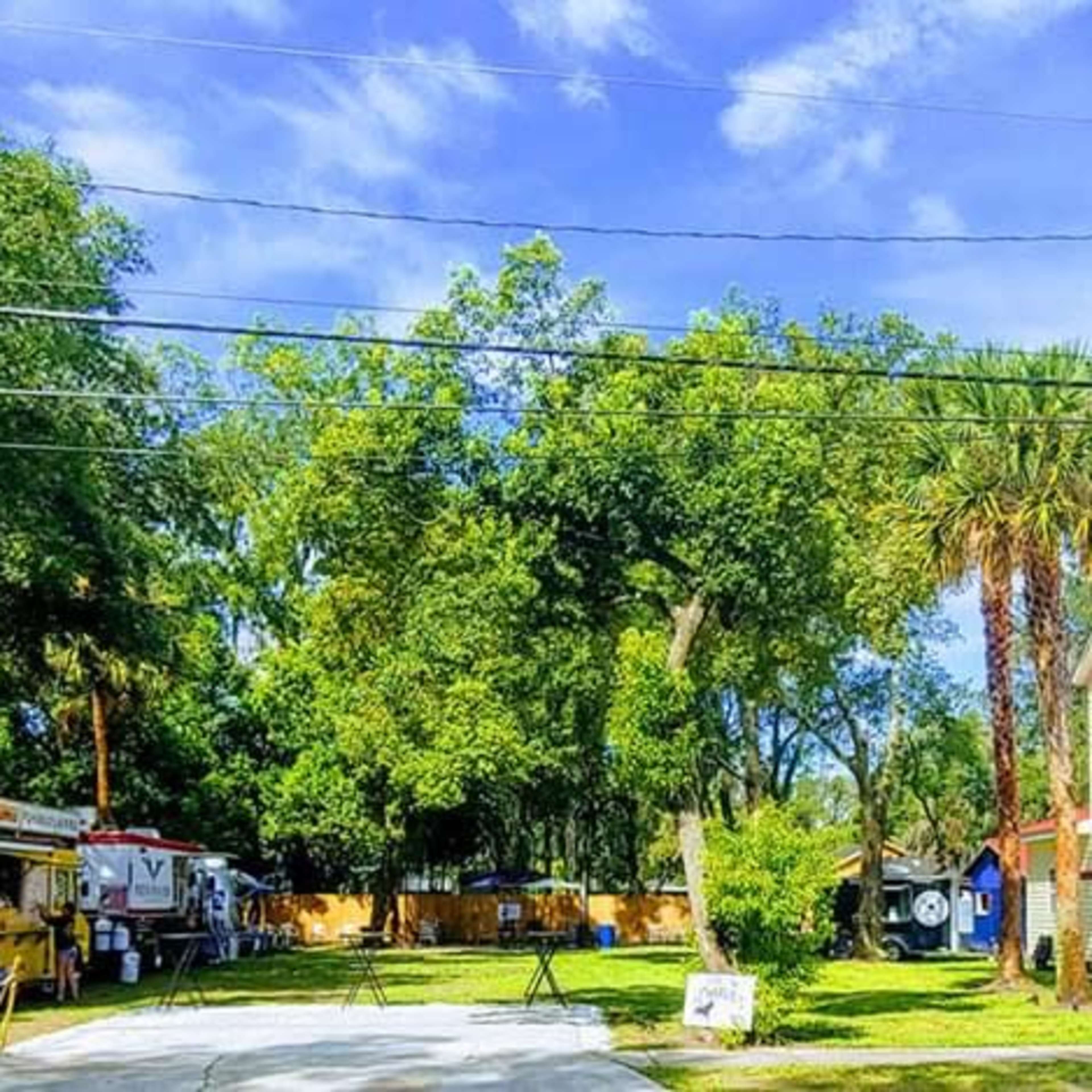 A white two-story house with a red roof is situated on a tree-lined street alongside a food truck and several large trees.