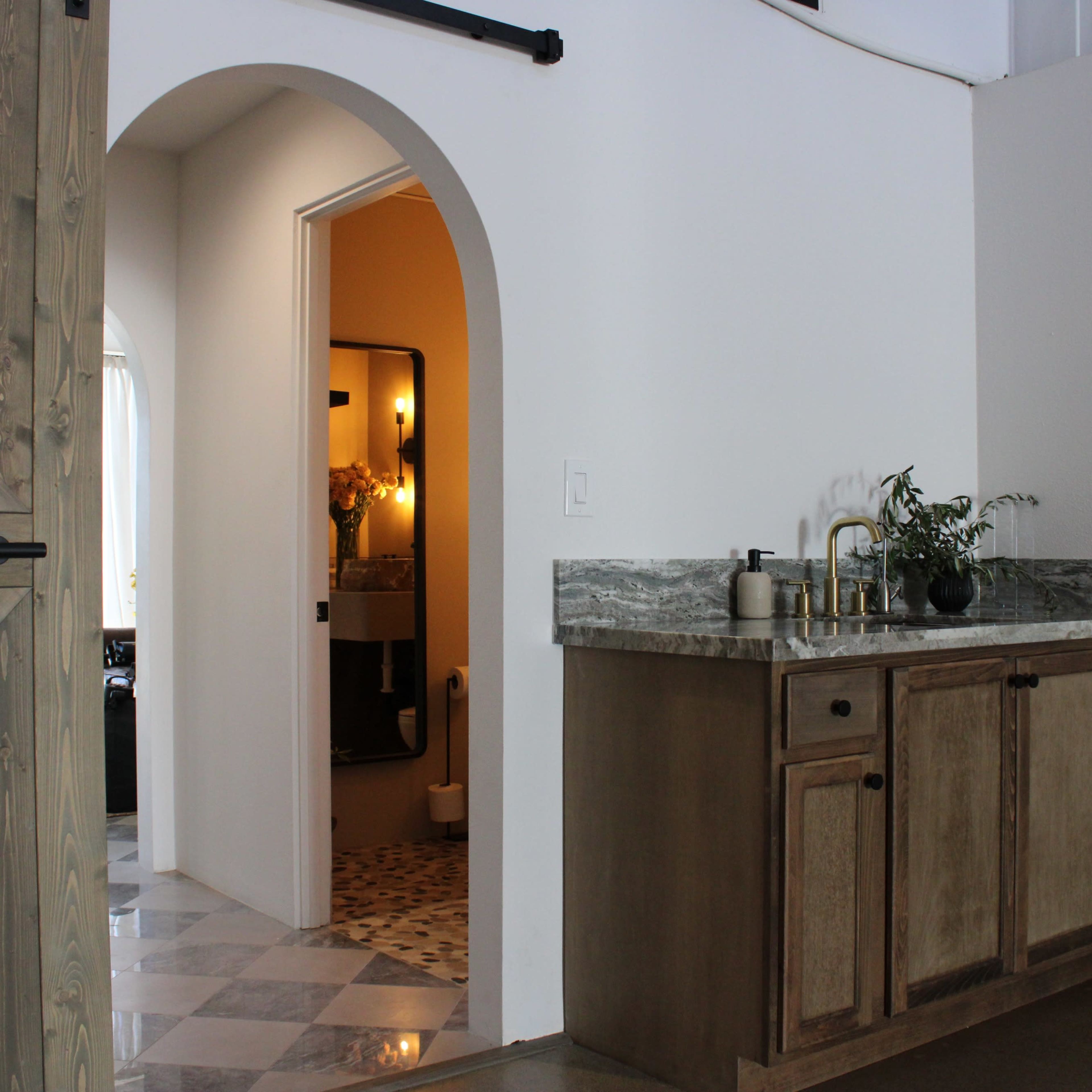 A modern interior space featuring a wooden bar with a granite countertop, an arched doorway leading to a bathroom, and patterned tile flooring.