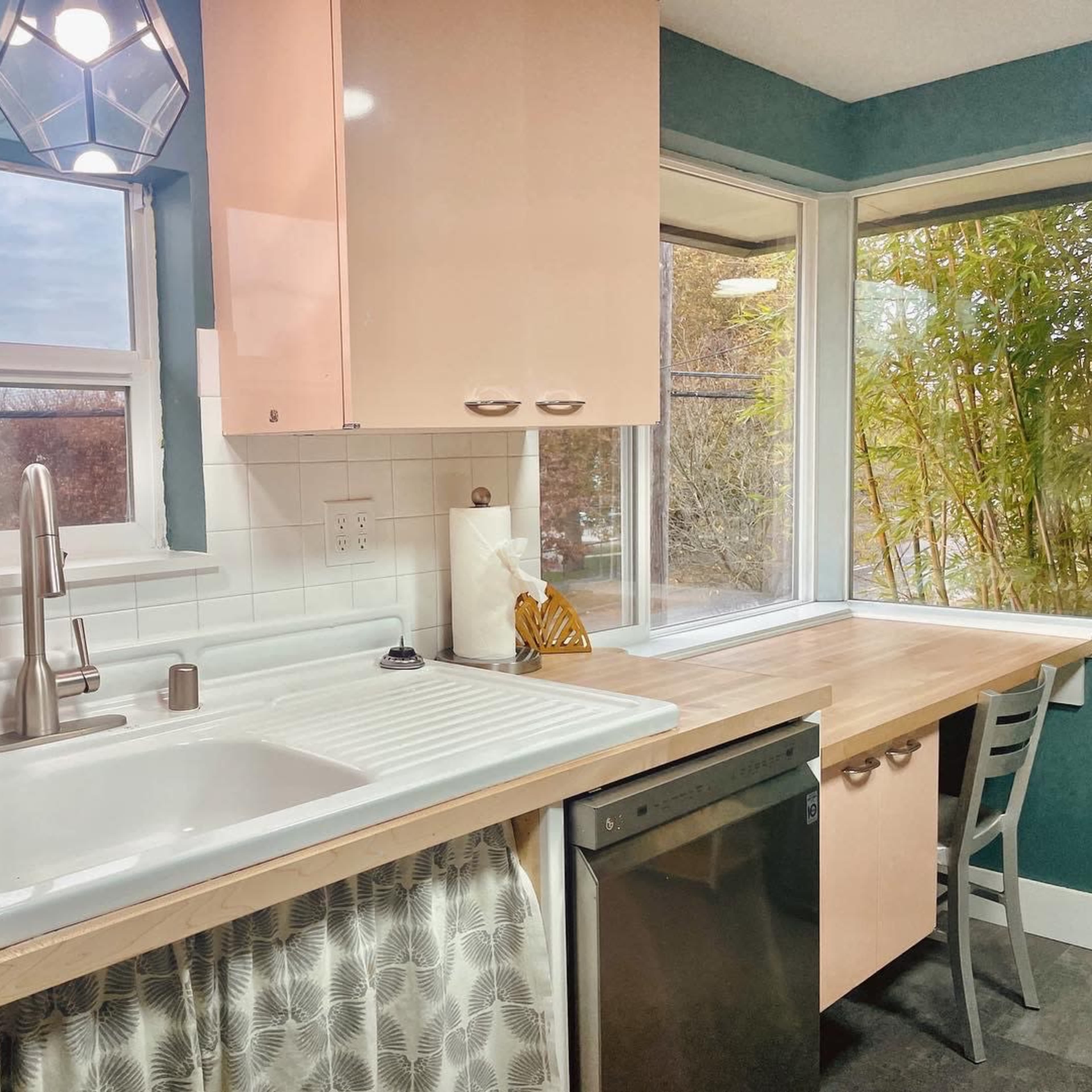 A modern kitchen features a double sink with a window view, light-colored cabinets, and a wooden countertop by a dining area.