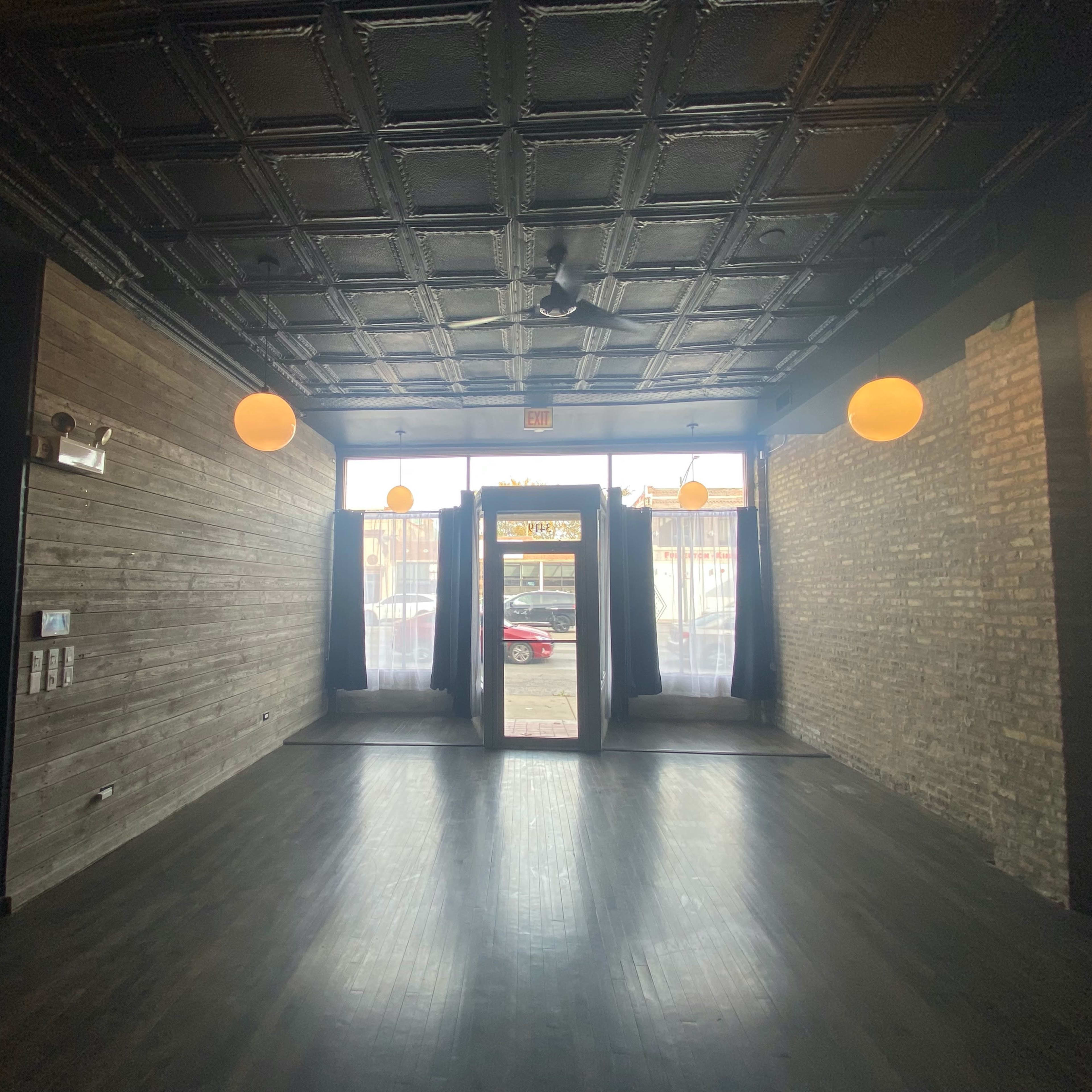 An empty room with a black ceiling, wooden walls, and a doorway flanked by dark curtains, leading to a bright exterior space.
