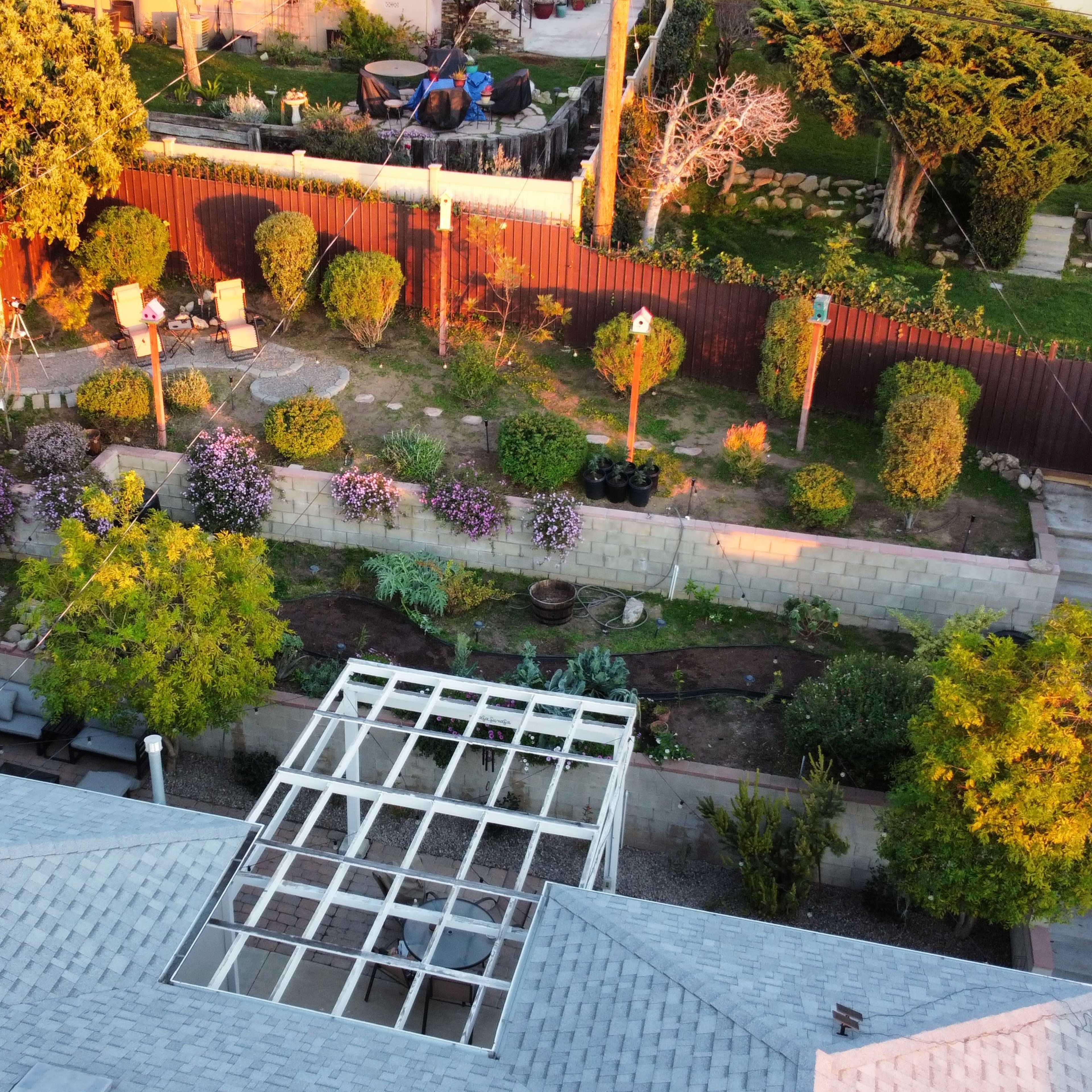 An aerial view of a garden with well-maintained shrubs, flower beds, and seating areas surrounded by a fence.