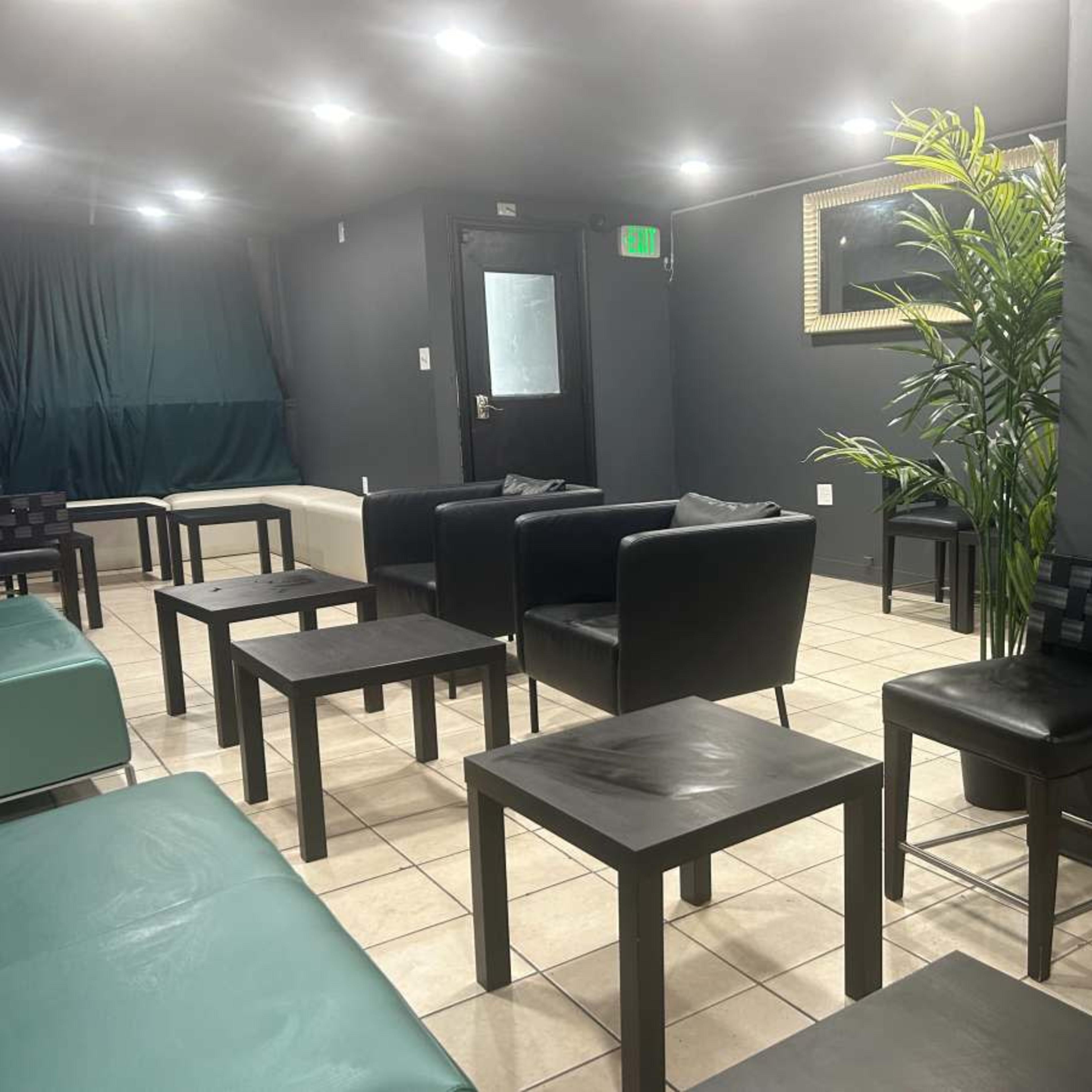 A modern lounge area with black and white furniture, including chairs and tables, against a backdrop of gray walls and dim lighting.